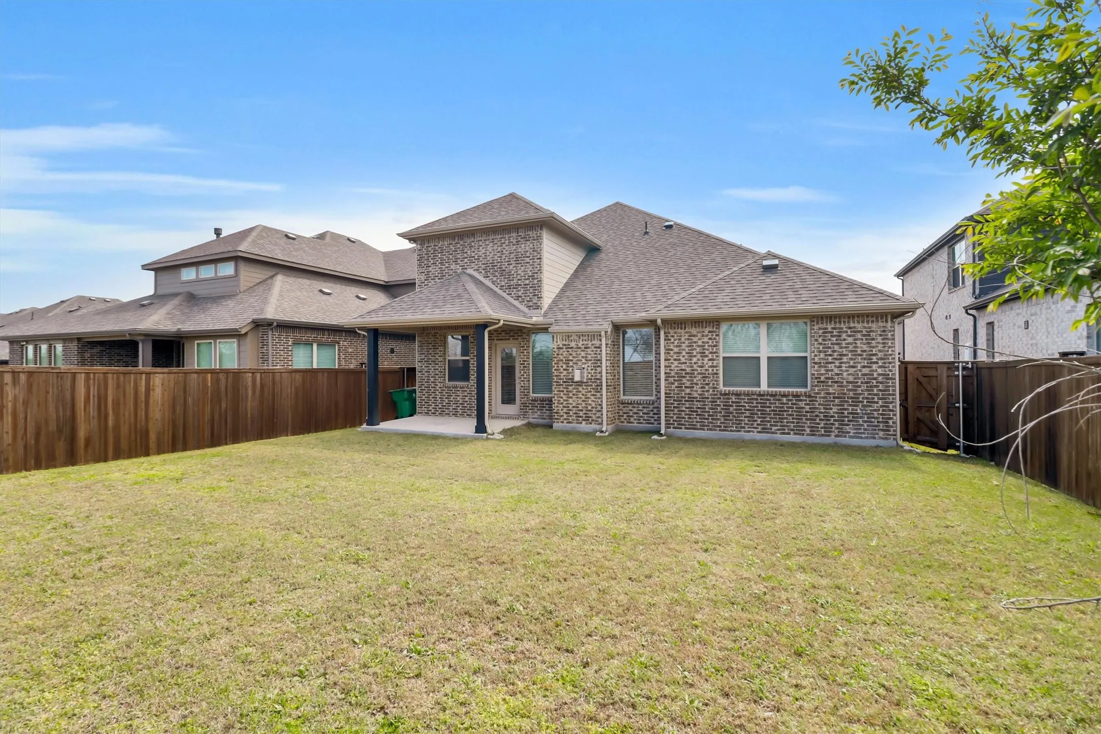 Expansive backyard featuring a manicured lawn, full privacy fencing, and a covered patio with direct house access