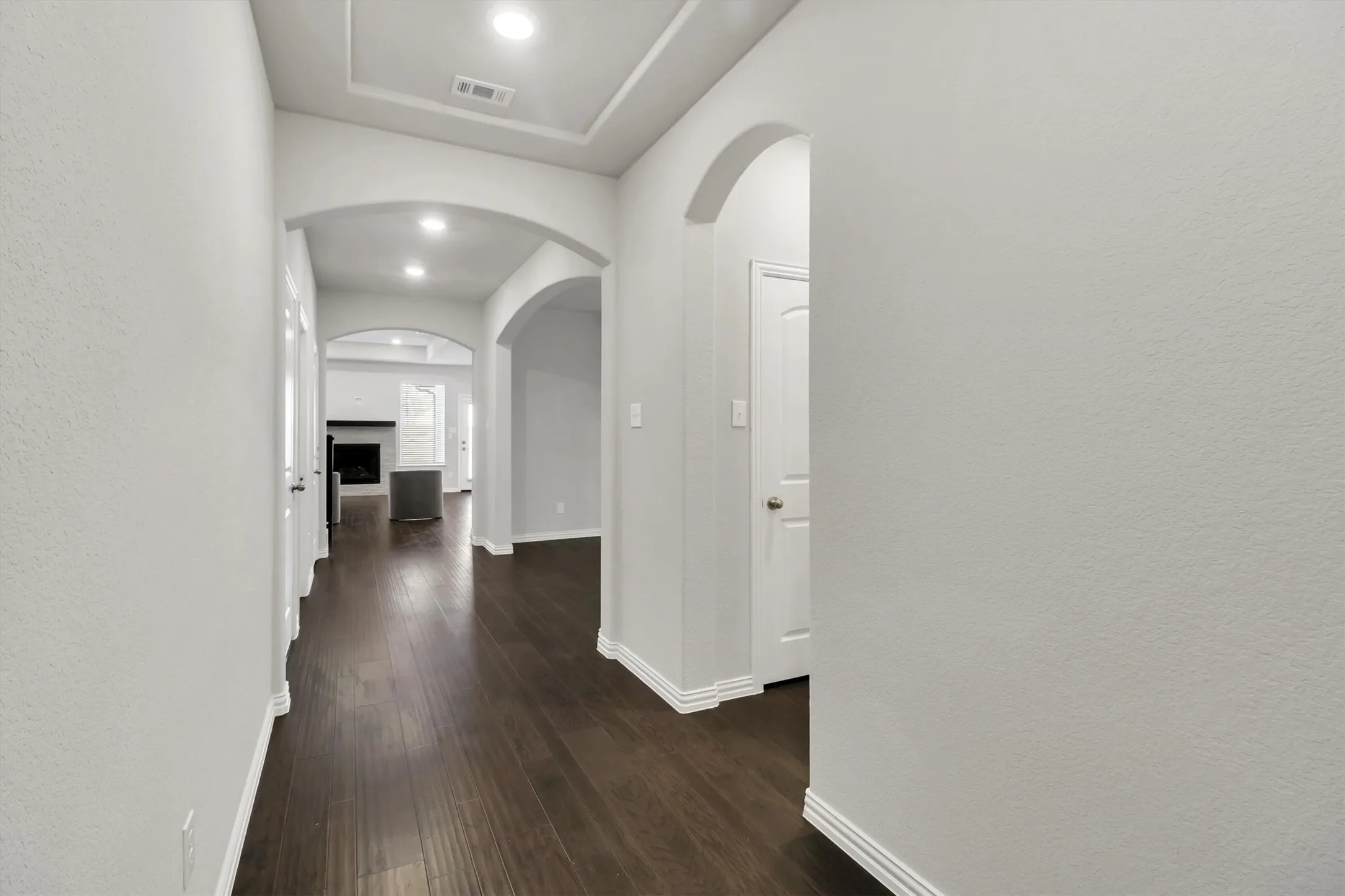 Hallway featuring wood-finish flooring, arched doorways, recessed lighting, and tray ceiling