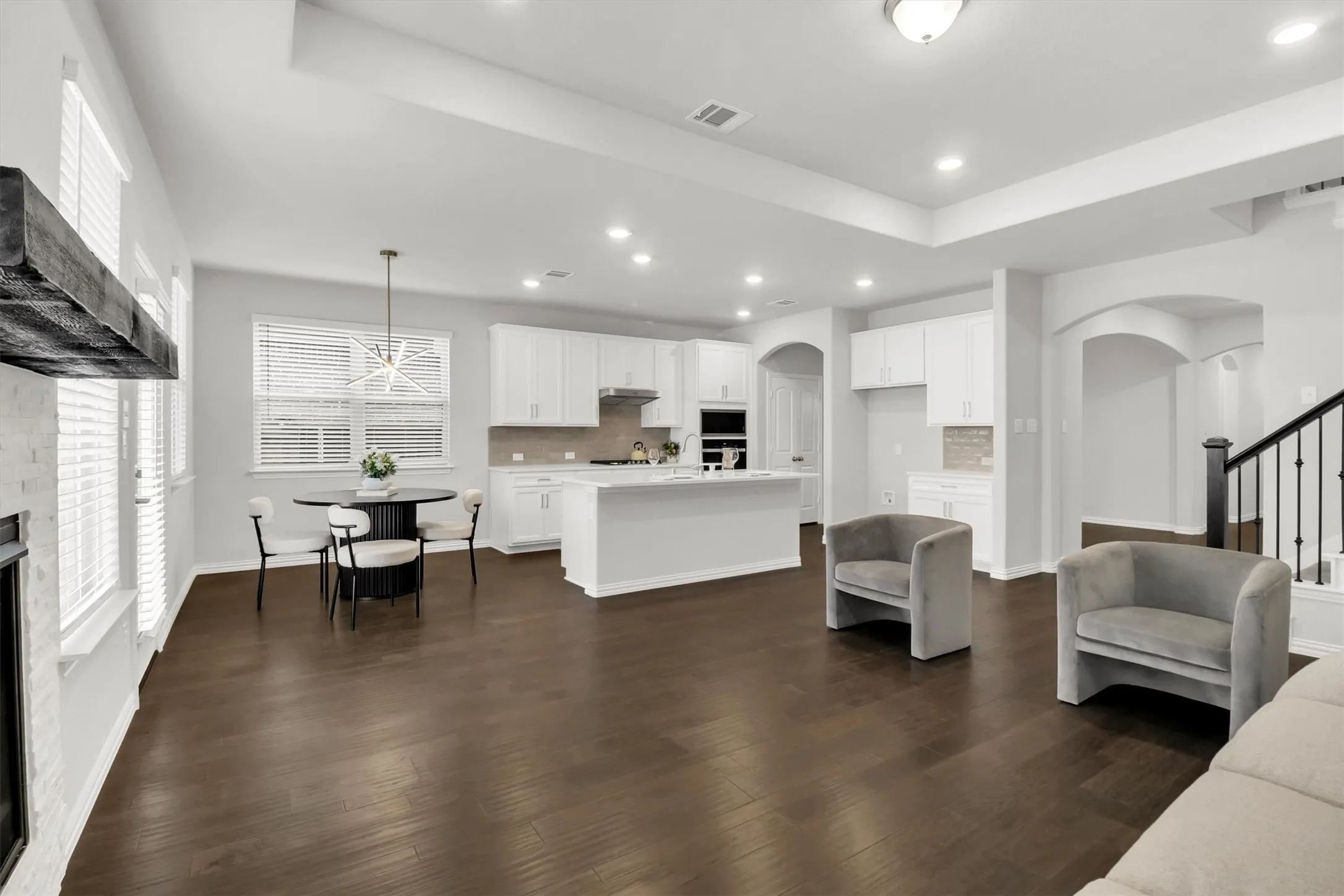 Open-concept living space featuring wood-finish flooring, recessed lighting, a white kitchen with an island, and an adjacent dining area