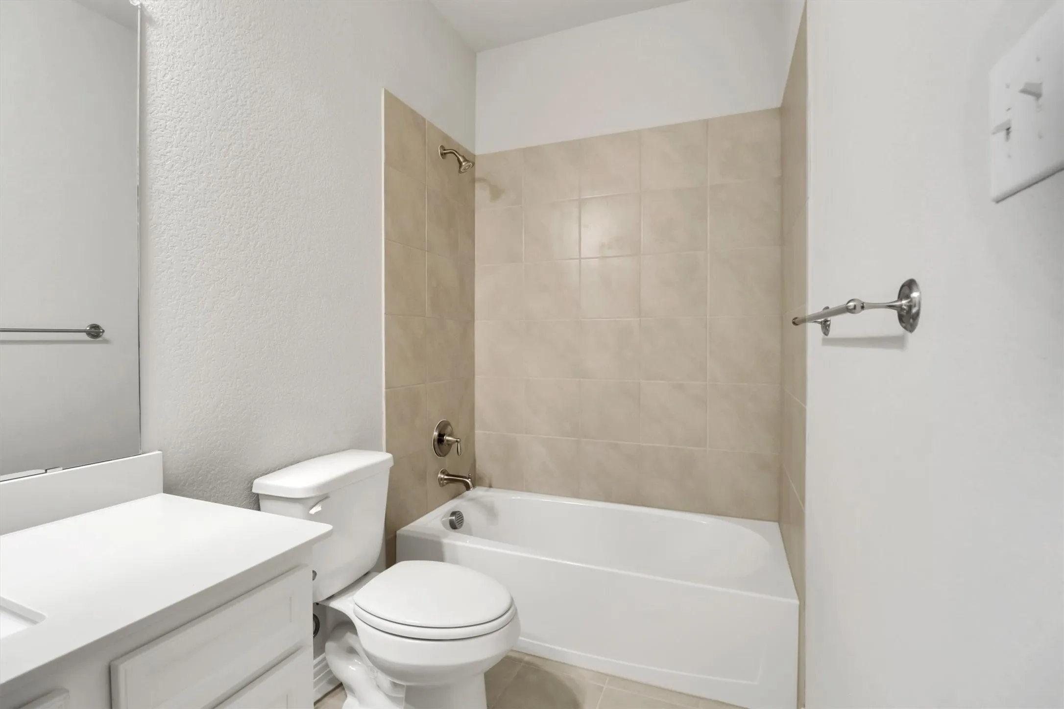 Bathroom featuring a white vanity with a countertop sink, a white toilet, and a bathtub with tile surround