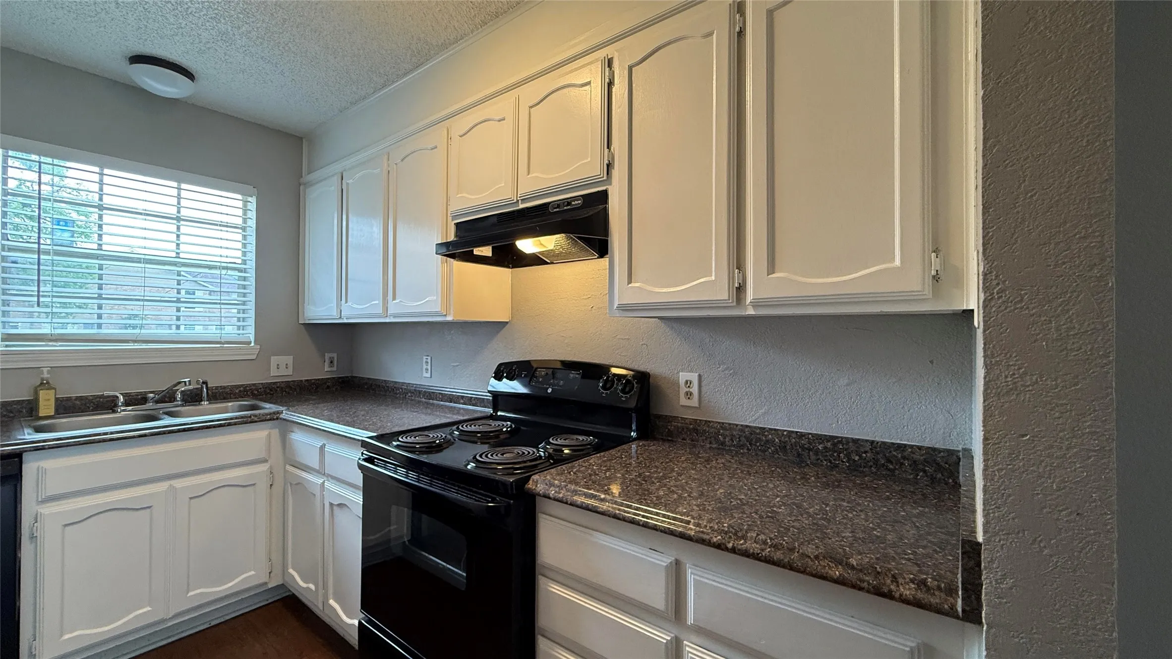 Kitchen featuring a sink, dark countertops, a textured ceiling, black / electric stove, and under cabinet range hood
