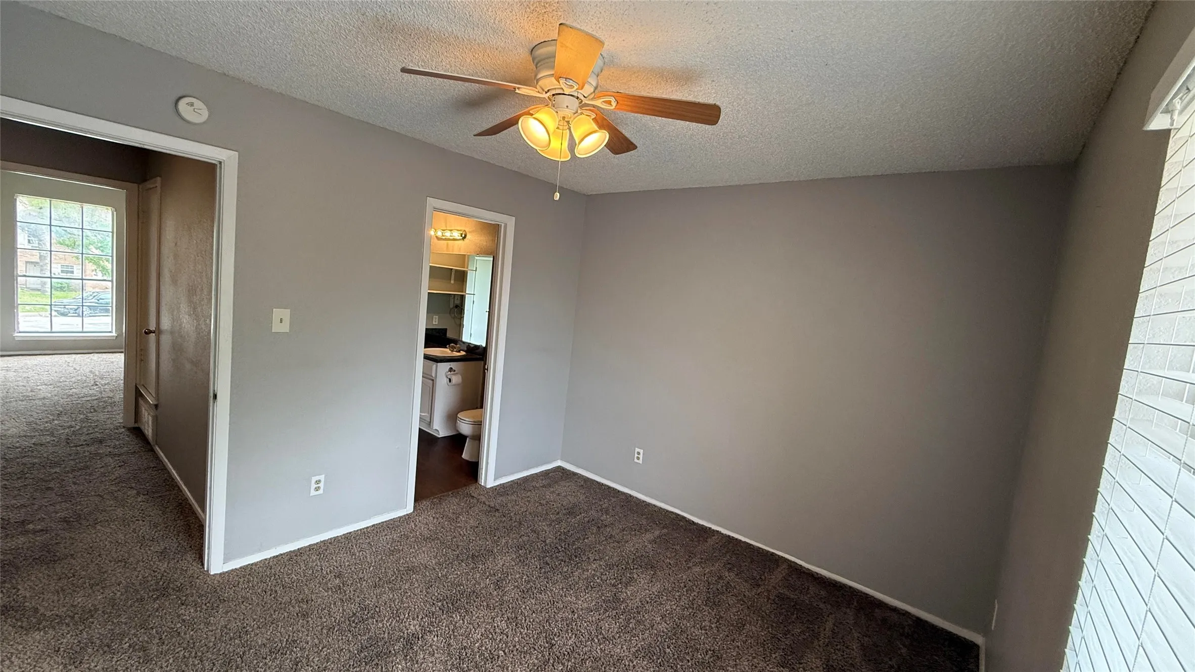 Unfurnished bedroom with a textured ceiling, ceiling fan, dark colored carpet, and baseboards