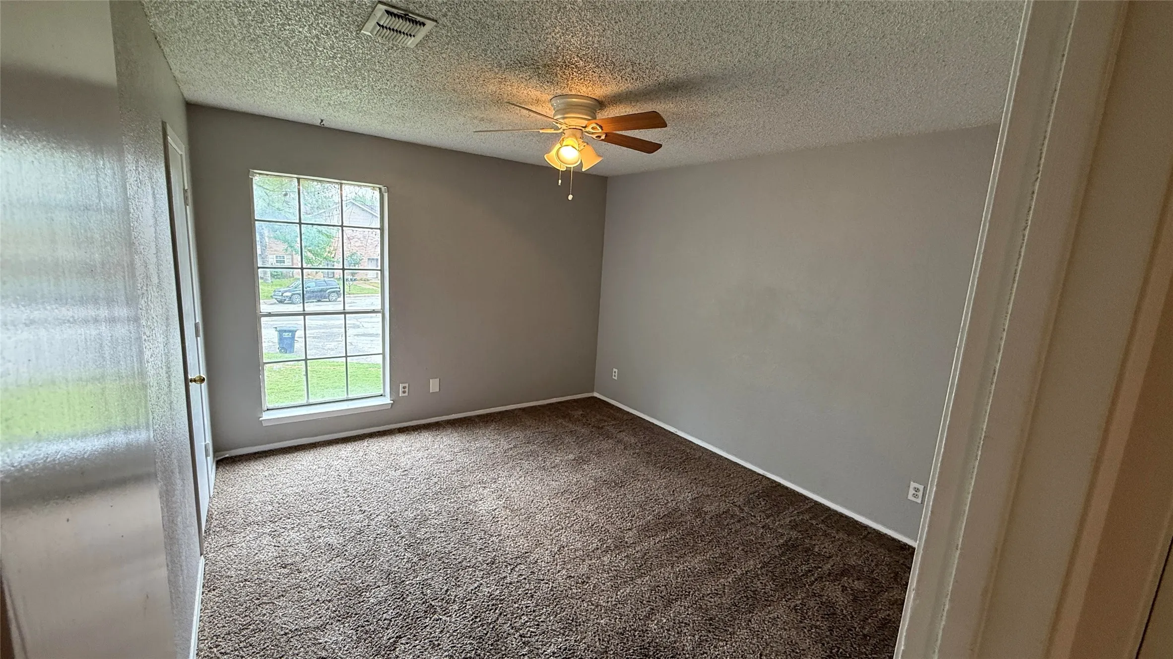 Carpeted spare room with visible vents, baseboards, a ceiling fan, and a textured ceiling