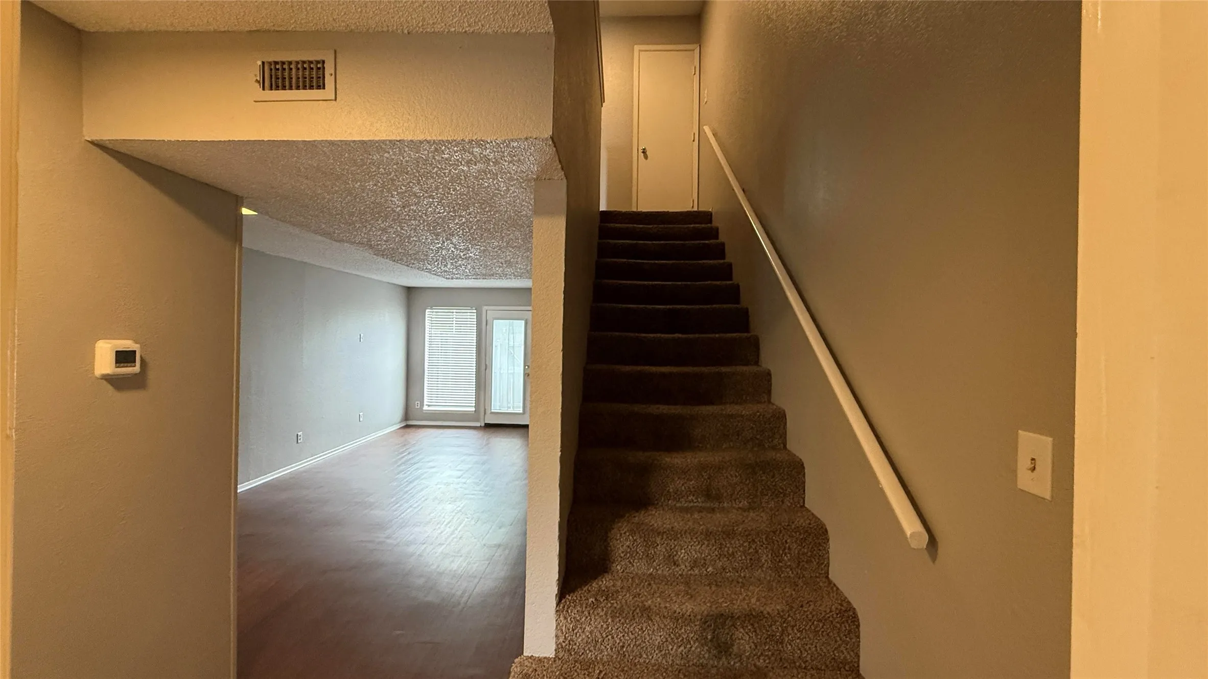 Stairway with a textured ceiling, wood finished floors, baseboards, and visible vents