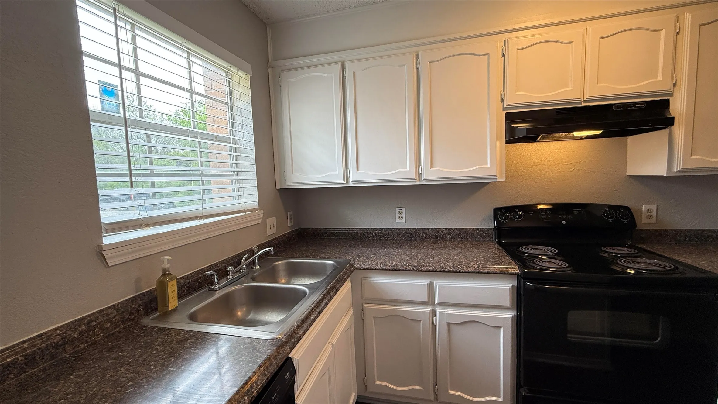 Kitchen with black electric range oven, under cabinet range hood, white cabinets, and a sink