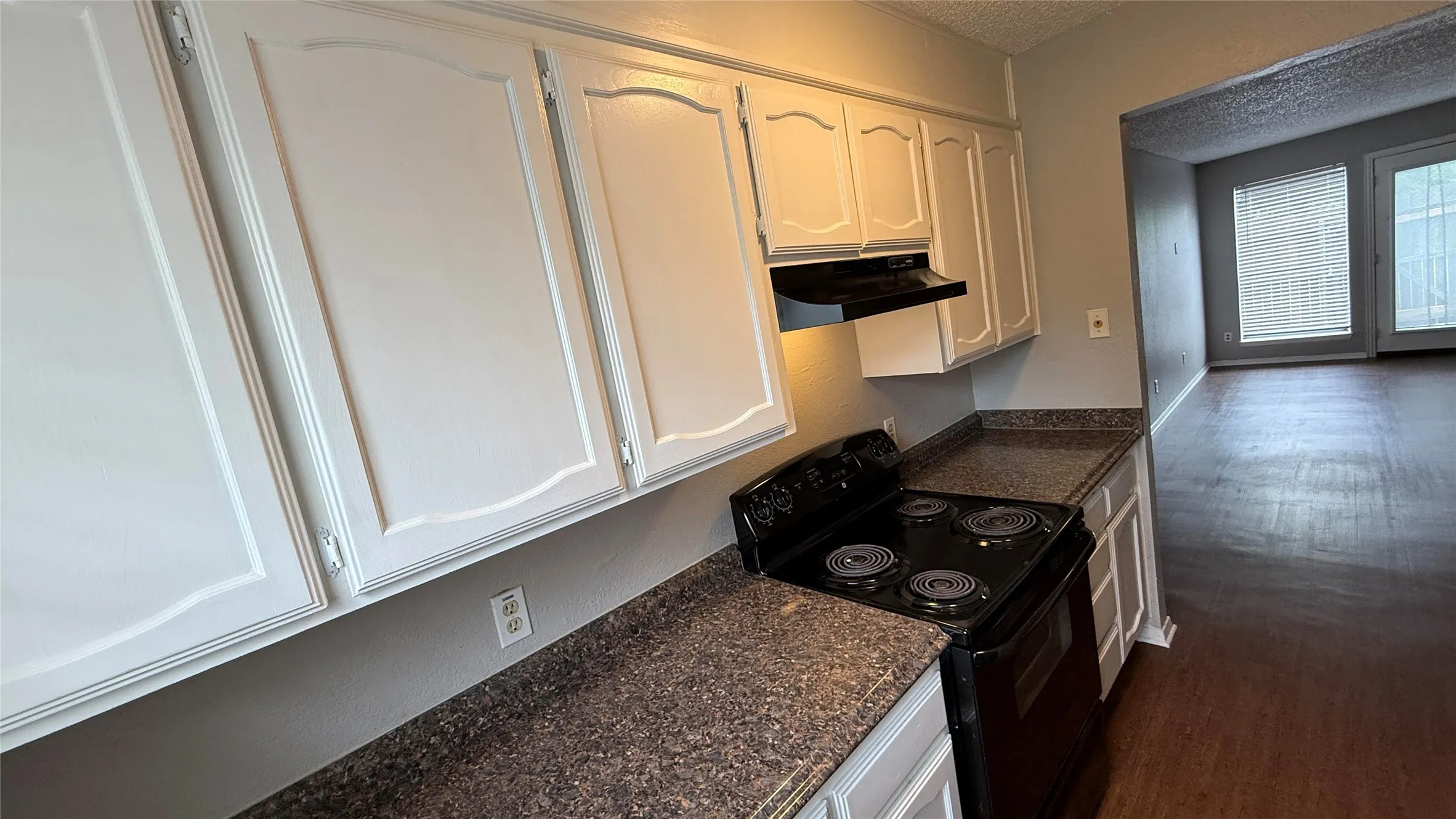 Kitchen featuring white cabinets, under cabinet range hood, black / electric stove, and a textured ceiling