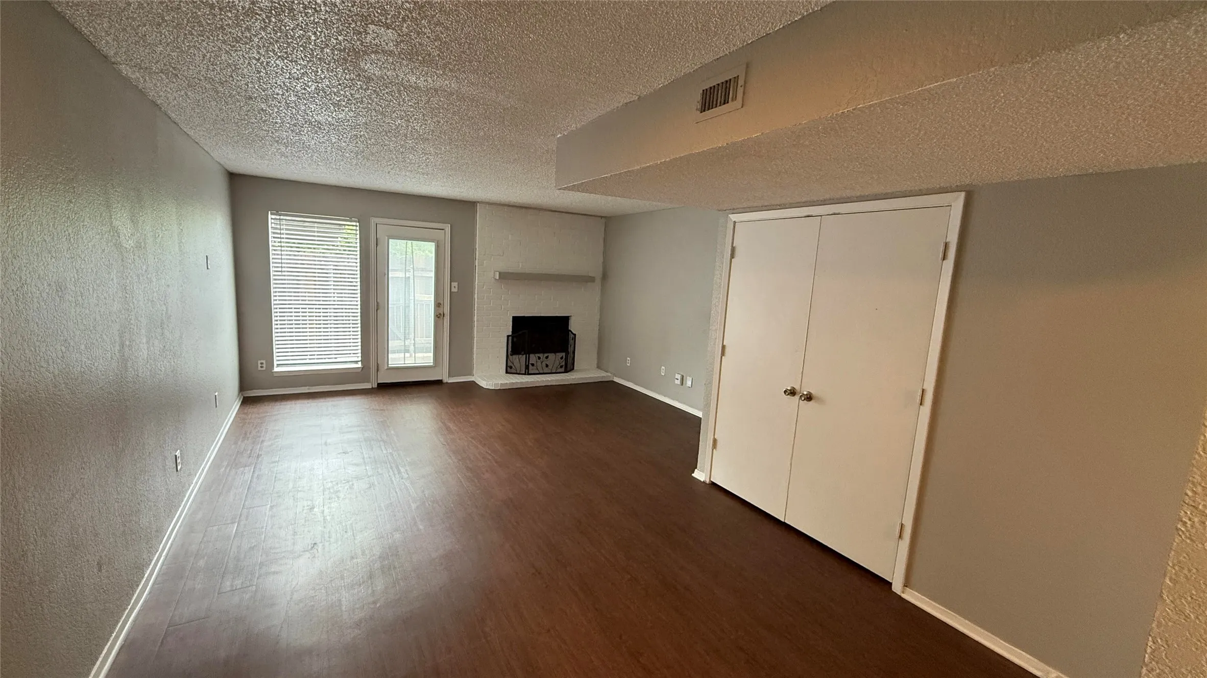 Unfurnished living room with dark wood-type flooring, a textured ceiling, visible vents, a textured wall, and baseboards