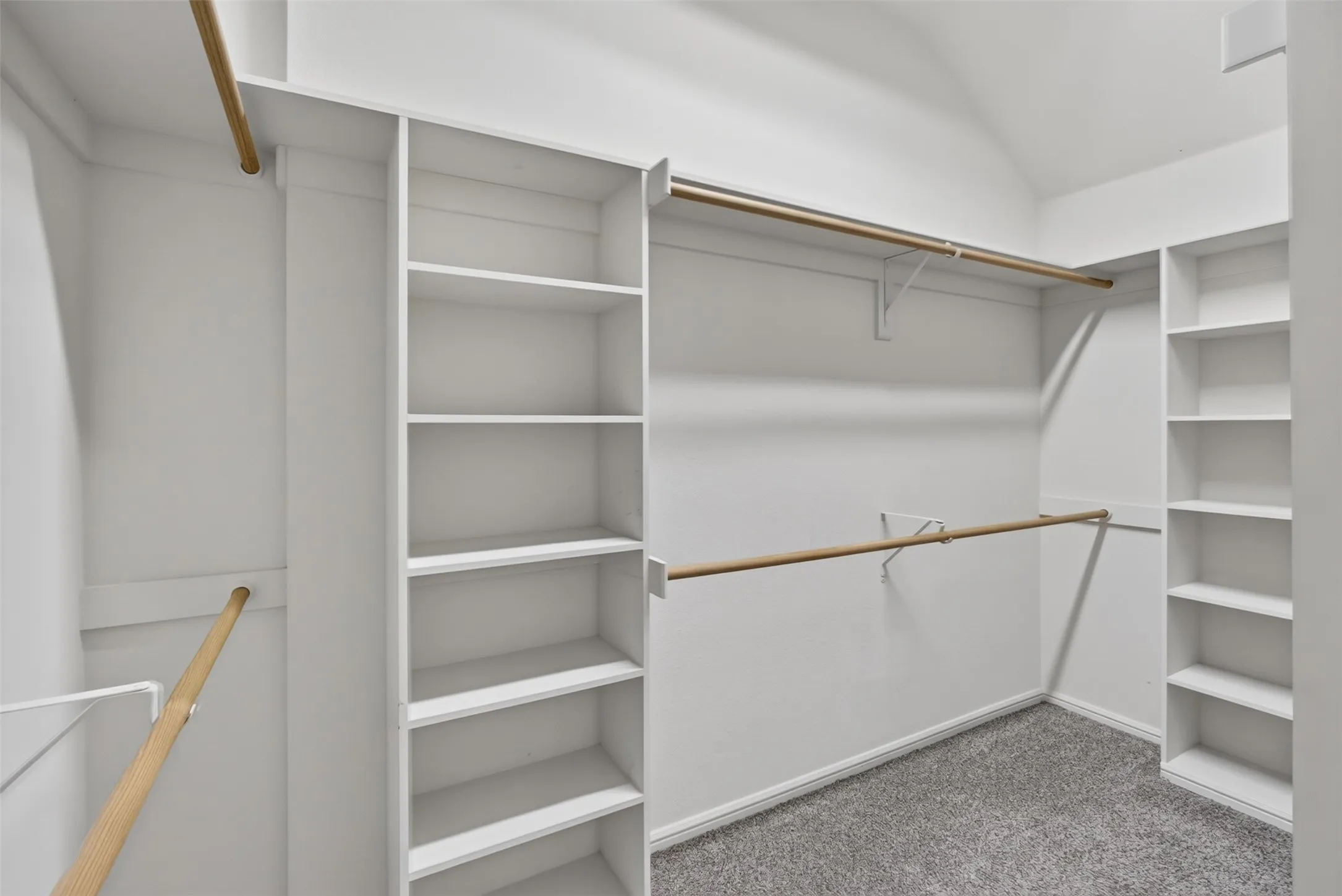 Master bedroom. Built-in shelving, multiple hanging rods, and gray carpet flooring.