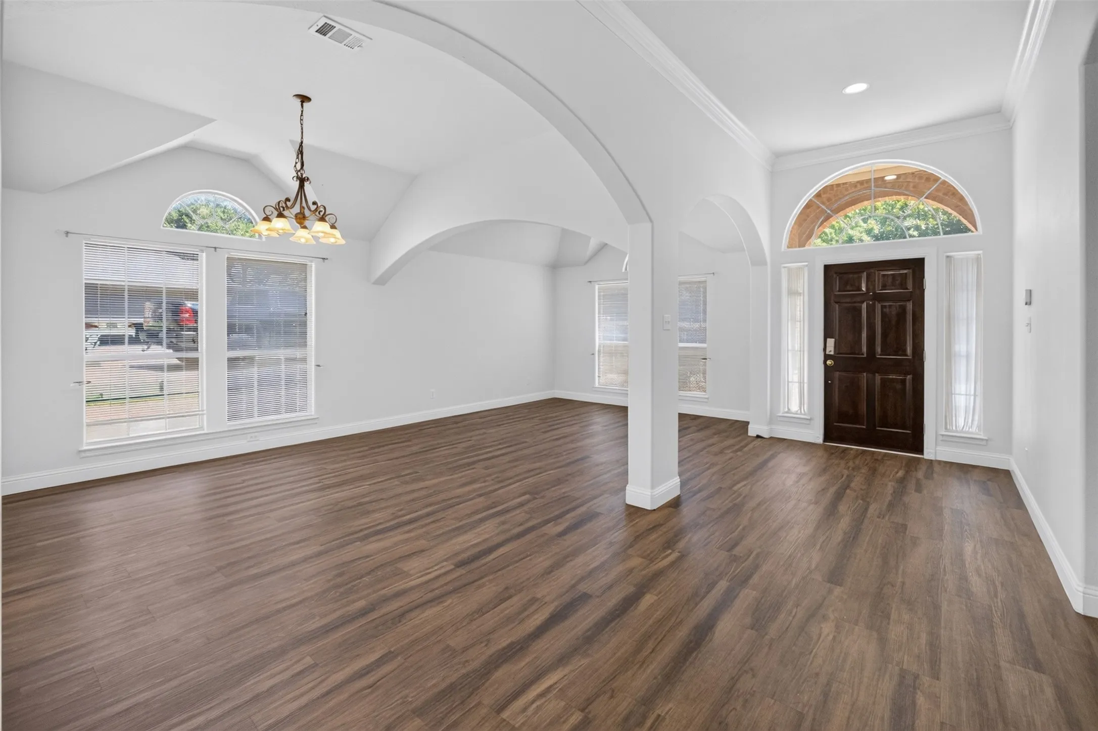 Spacious open-concept living area featuring soaring barrel-vaulted ceilings with exposed structural columns, warm wood-finish flooring throughout, and abundant natural light from large multi-pane windows