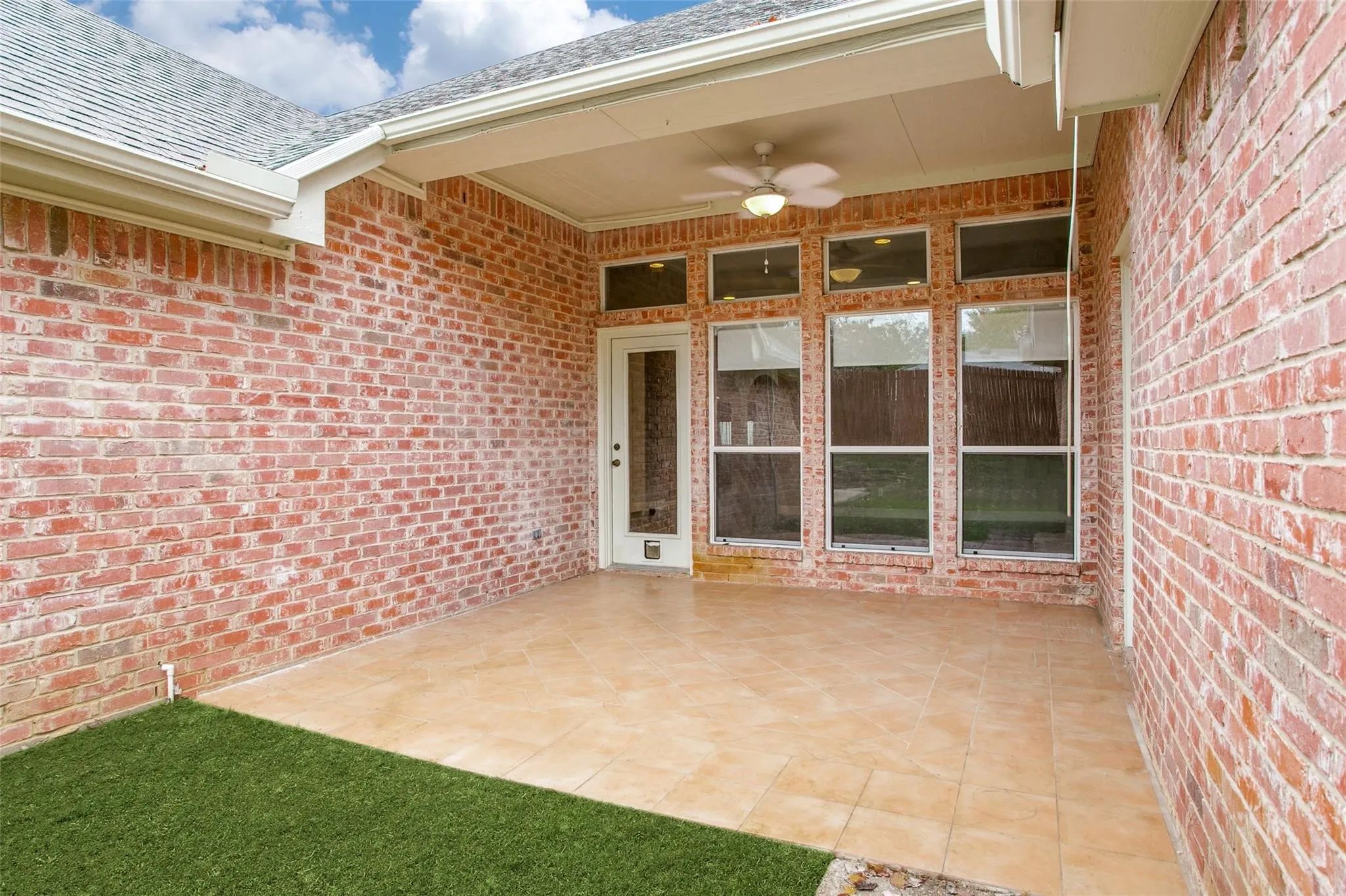 Covered patio with a ceiling fan, tiled flooring, and brick exterior walls