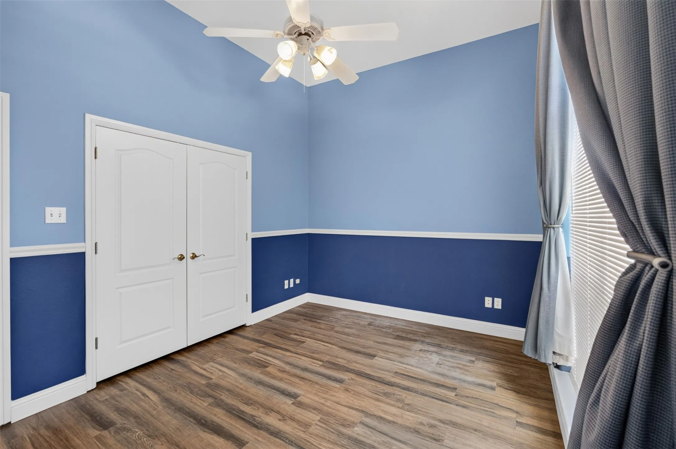 Vaulted ceiling with a ceiling fan, wood-finish flooring, two-tone wall treatment, and white interior doors. Walk in closet.