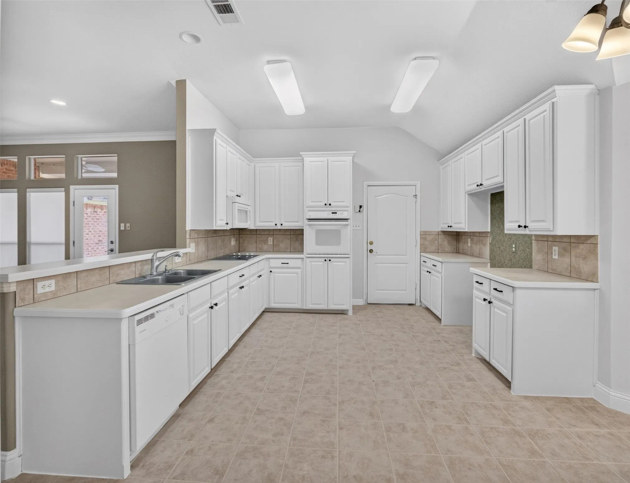 Kitchen featuring extensive white cabinetry, light-toned countertops, a tile backsplash, and a double basin sink