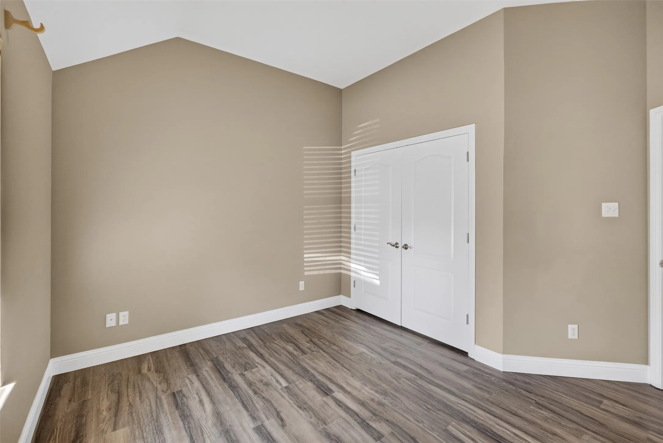 Vaulted ceiling, wood-finish flooring, neutral paint, white trim, and white double doors.