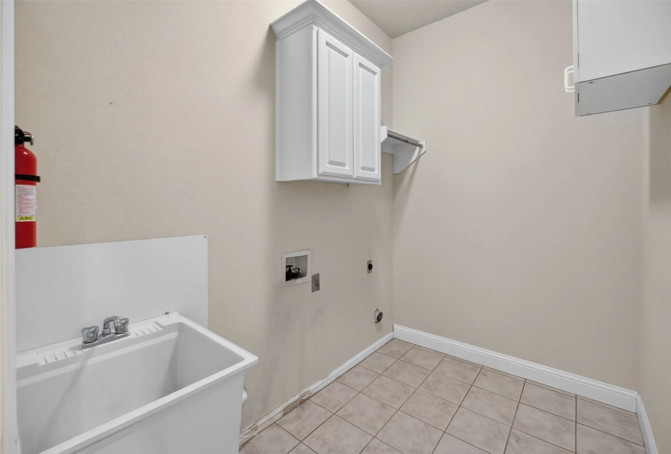 Utility space with a built-in white sink, chrome faucet, tiled flooring, and wall-mounted cabinetry.