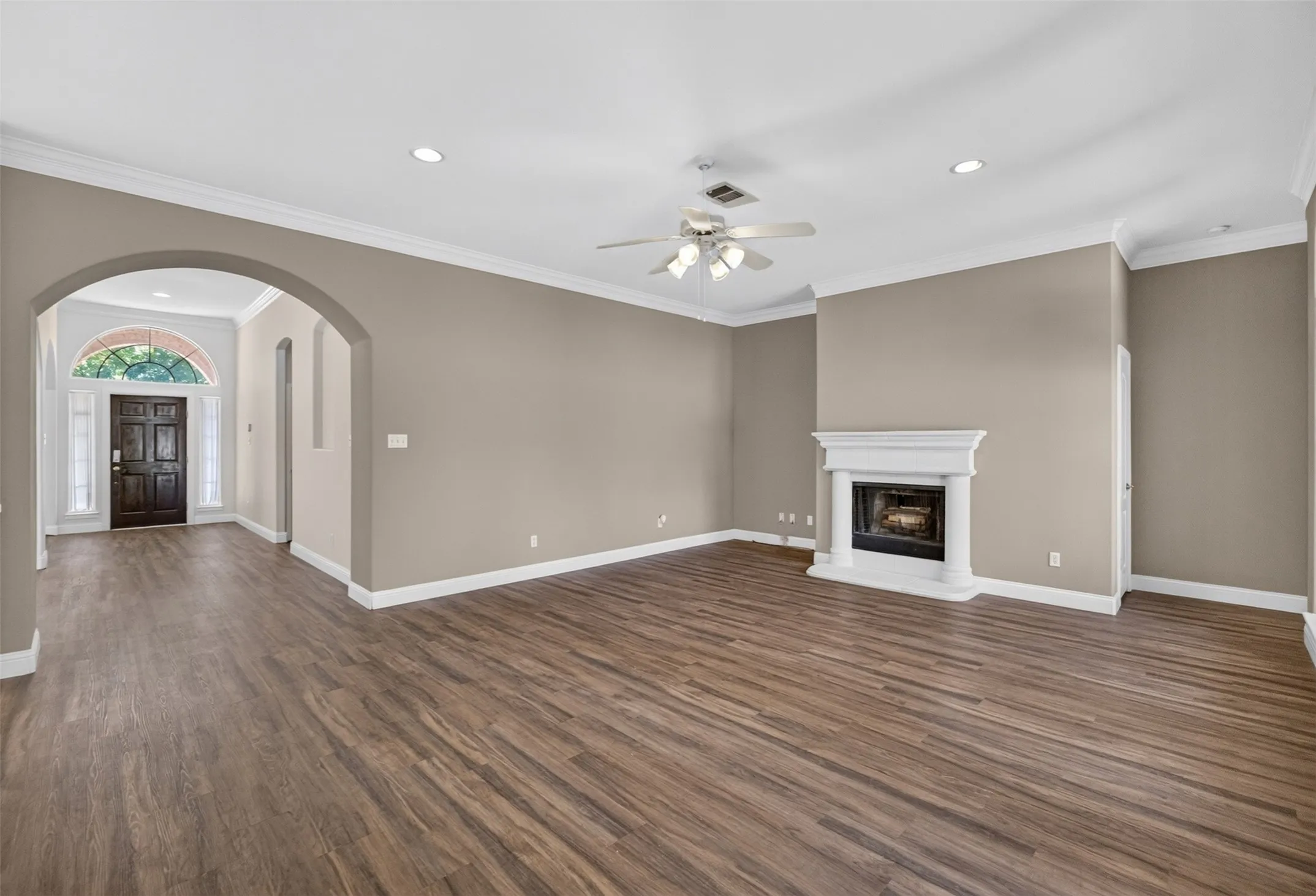 Spacious living area featuring wood-finish flooring, a white fireplace with a mantel, and crown molding.