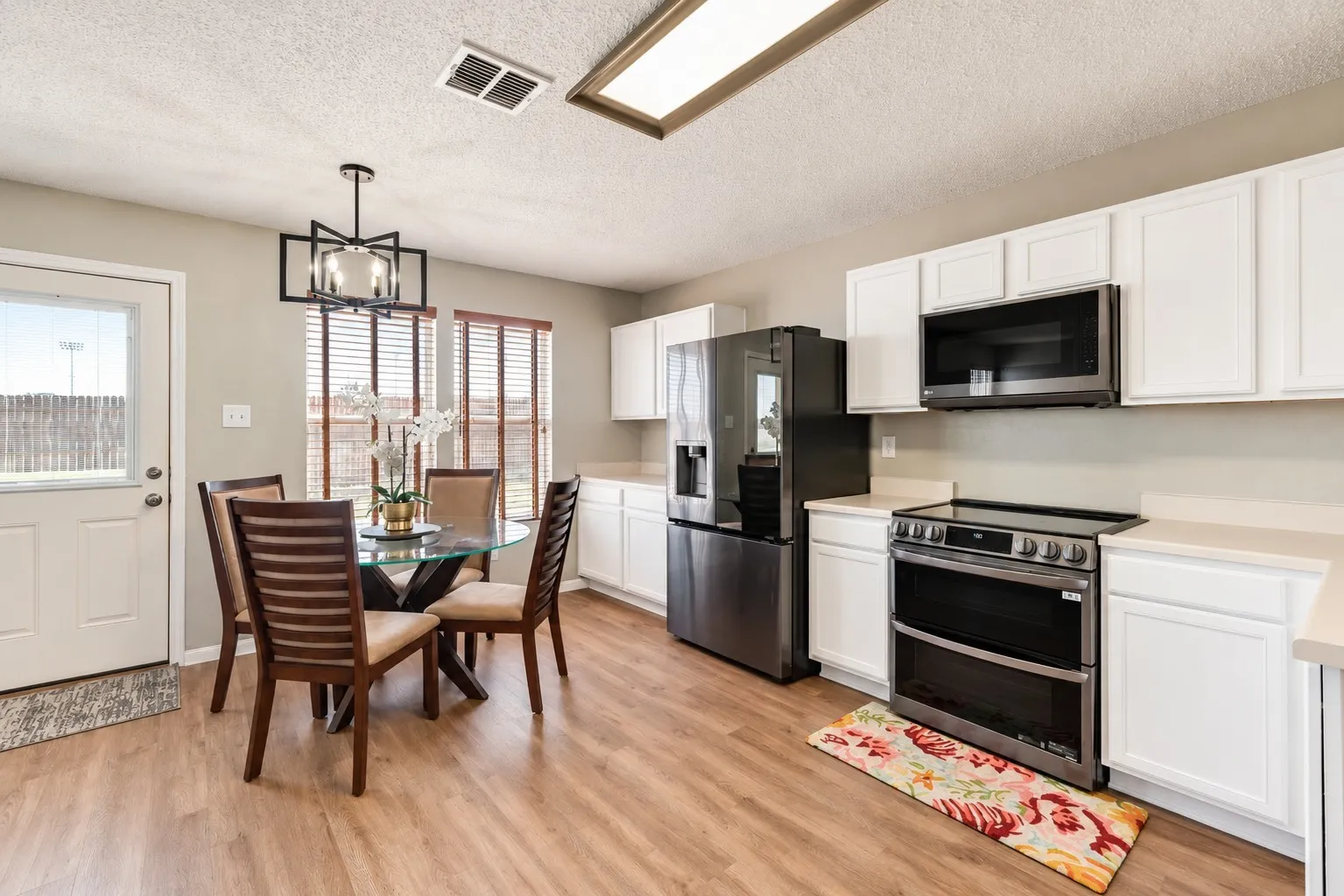 Modern kitchen featuring white cabinetry, light countertops, wood-finish flooring, and a contemporary pendant light fixture