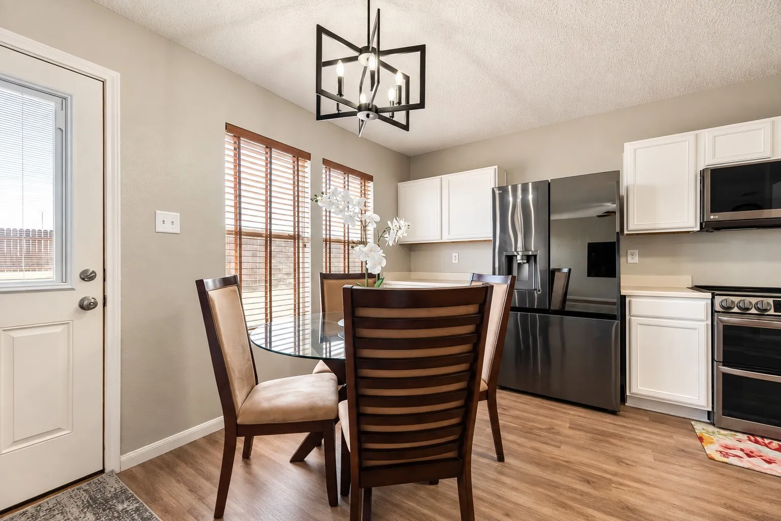 Kitchen dining area featuring wood-finish flooring, white cabinetry, stainless steel appliances, a geometric chandelier, and wood-slatted window blinds