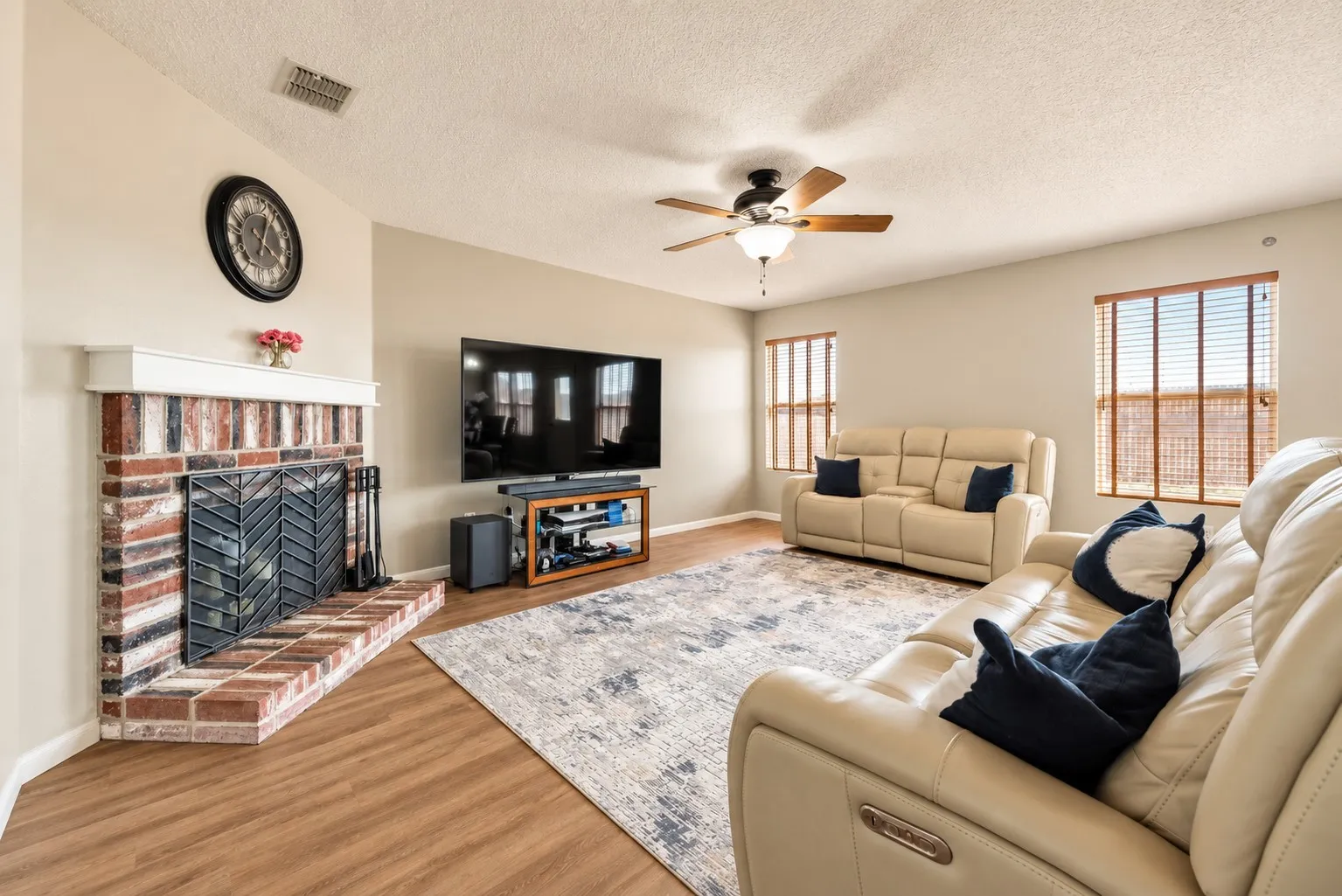 Corner brick fireplace with white mantel, wood-finish flooring, and a ceiling fan with integrated lighting