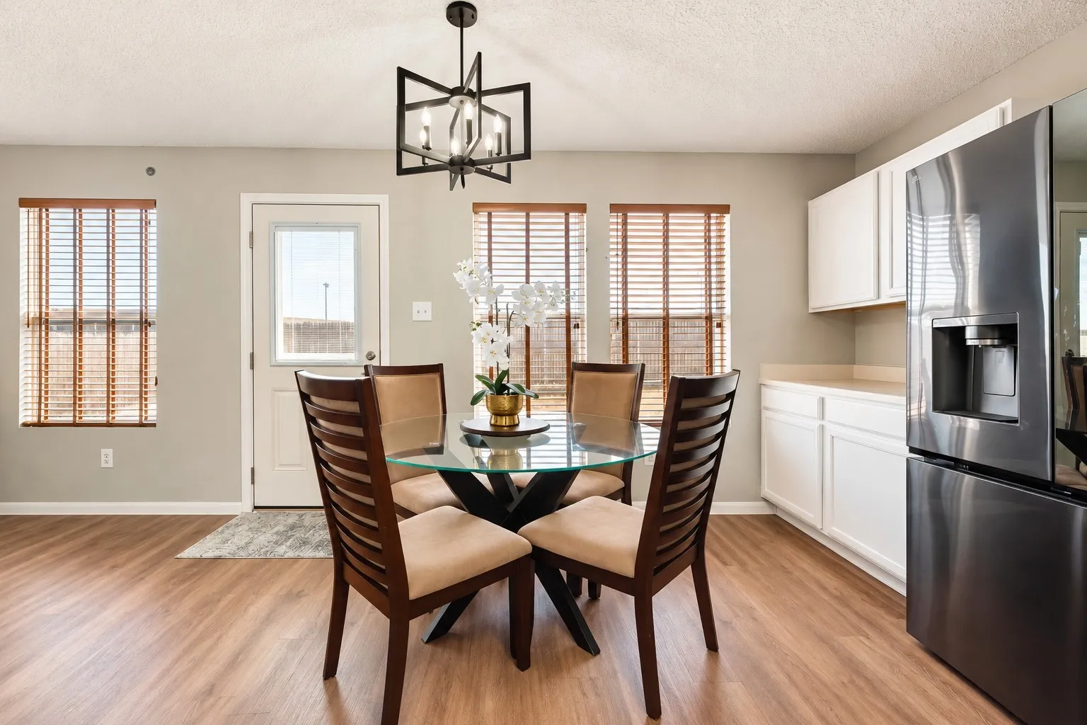 Wood-finish flooring, white cabinetry, stainless steel refrigerator, and a modern ceiling light fixture