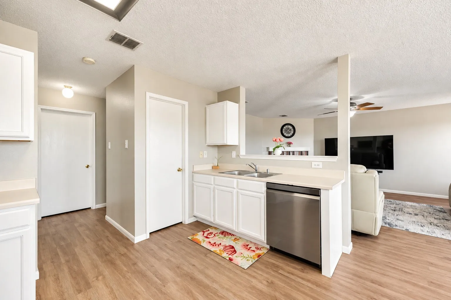 Kitchen featuring wood-finish flooring, white cabinetry, light-toned countertops, a stainless steel dishwasher, and a double basin sink