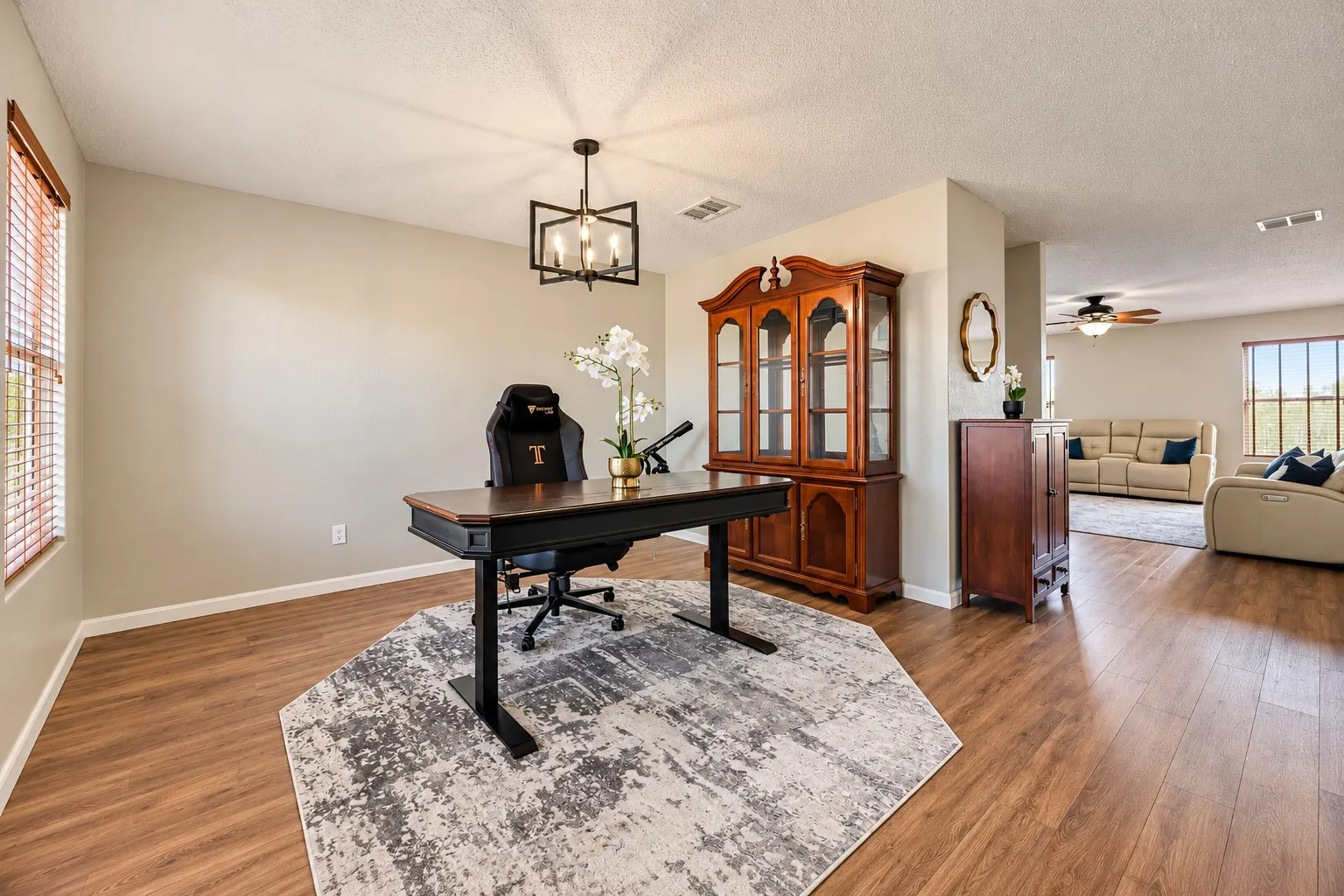 Wood-finish flooring throughout, with a window featuring wood-slat blinds, and a contemporary black metal chandelier