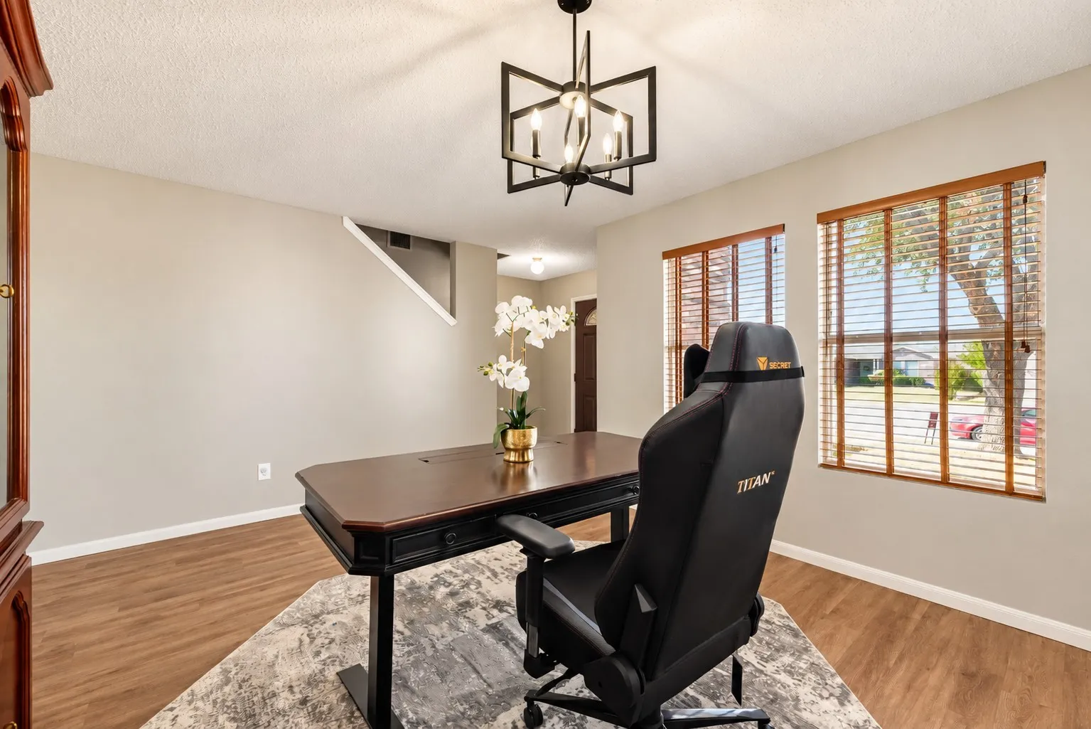 Neutral wall color, wood-finish flooring, two windows with wood blinds, and a geometric-frame chandelier