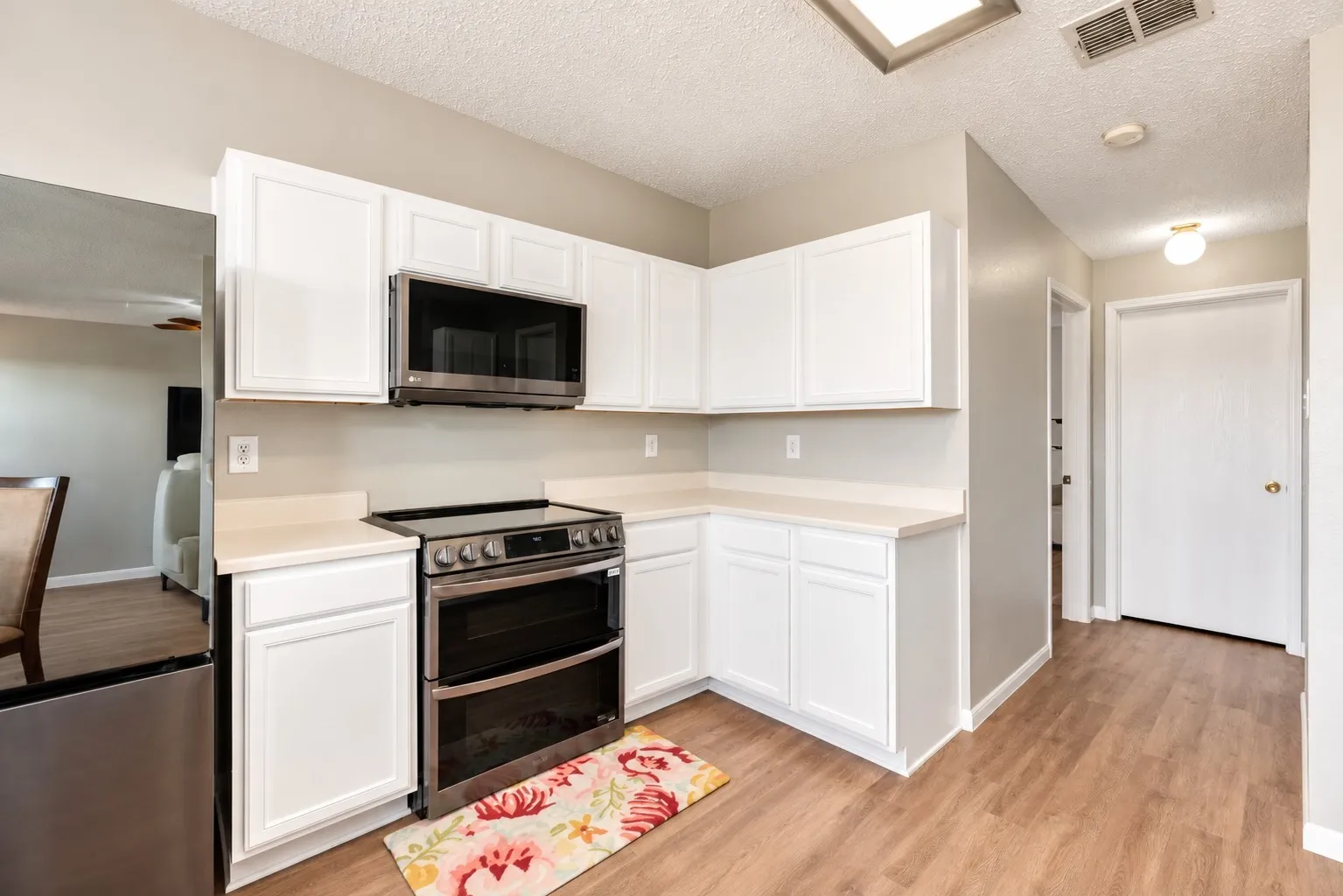 White cabinetry with light countertops, stainless steel electric range, built-in microwave, and wood-finish flooring