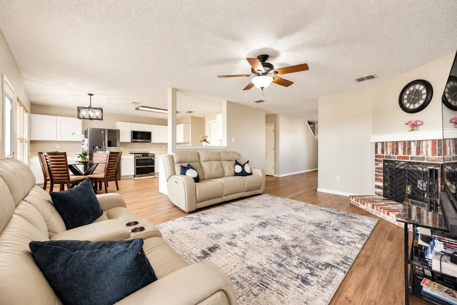 Open-concept living space featuring wood-finish flooring, a brick fireplace, and ceiling fan