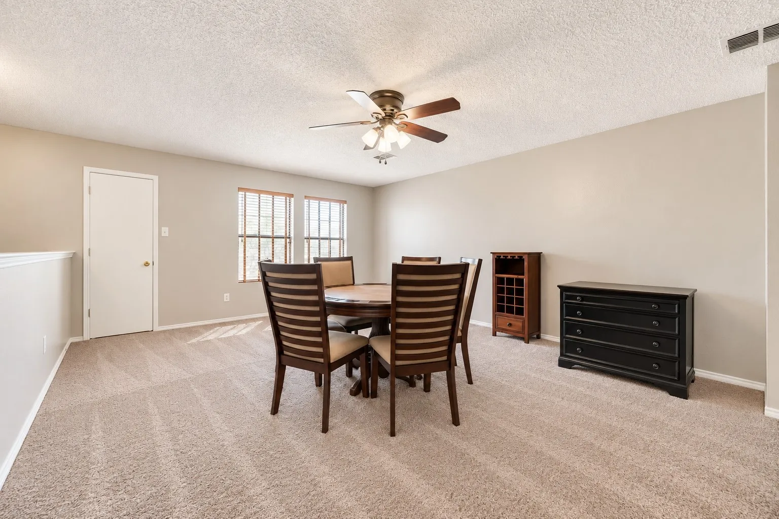 Spacious room featuring carpeting, neutral wall tones, two windows with blinds, and a ceiling fan with integrated lighting