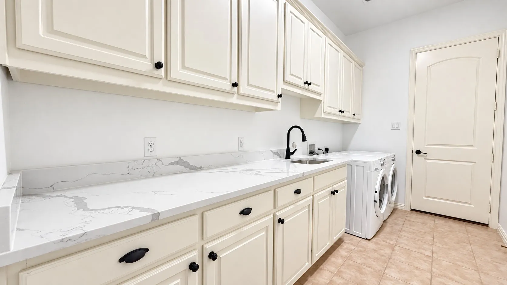 Extensive countertop space featuring a dual-basin sink, white shaker-style cabinetry with matte black hardware, and tiled flooring