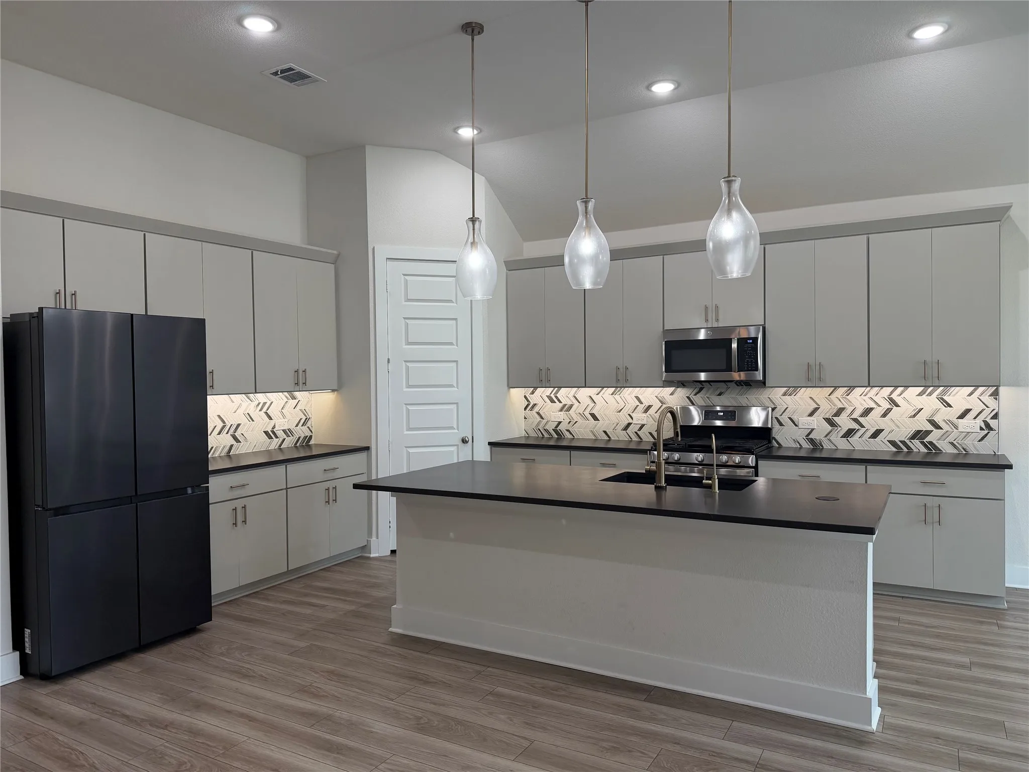 Wood-finish flooring, recessed lighting, ceiling fan, three windows with blinds, and a fireplace with a stone-tile surround and dark mantel