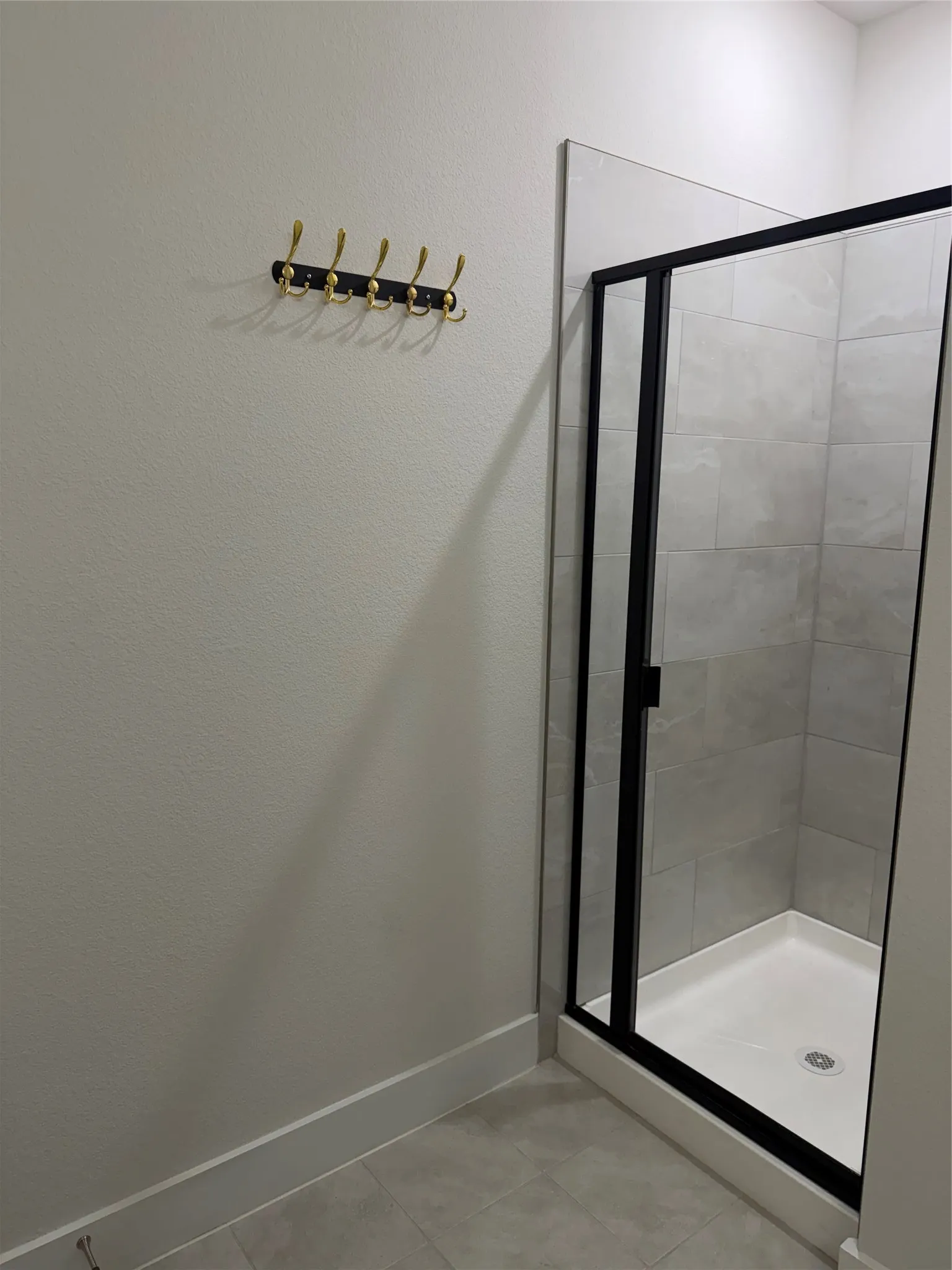 Enclosed shower with a black-framed glass door, light gray wall tile, and a white shower pan