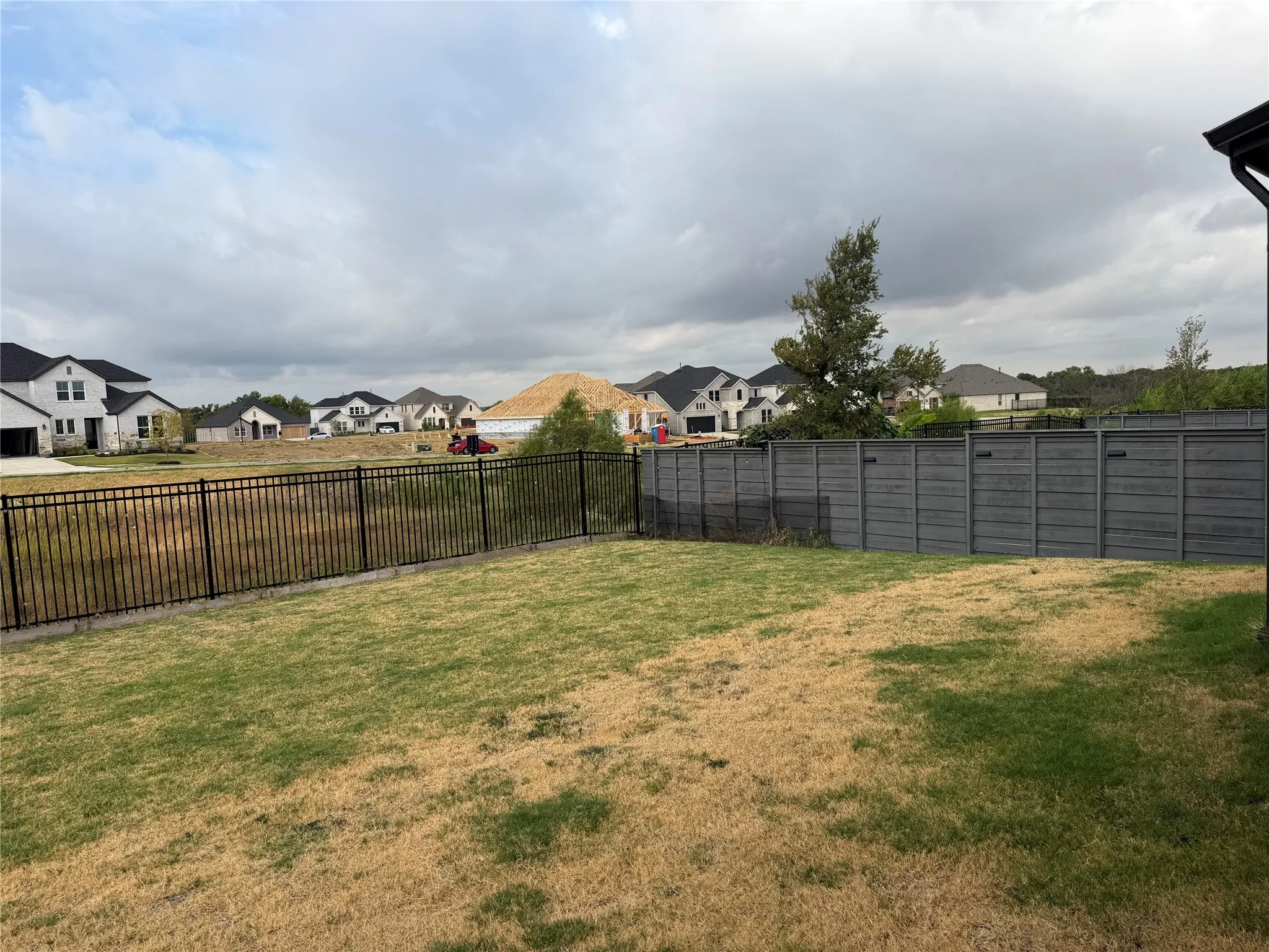 Expansive backyard featuring a wrought iron fence, a privacy fence, and a distant residential backdrop