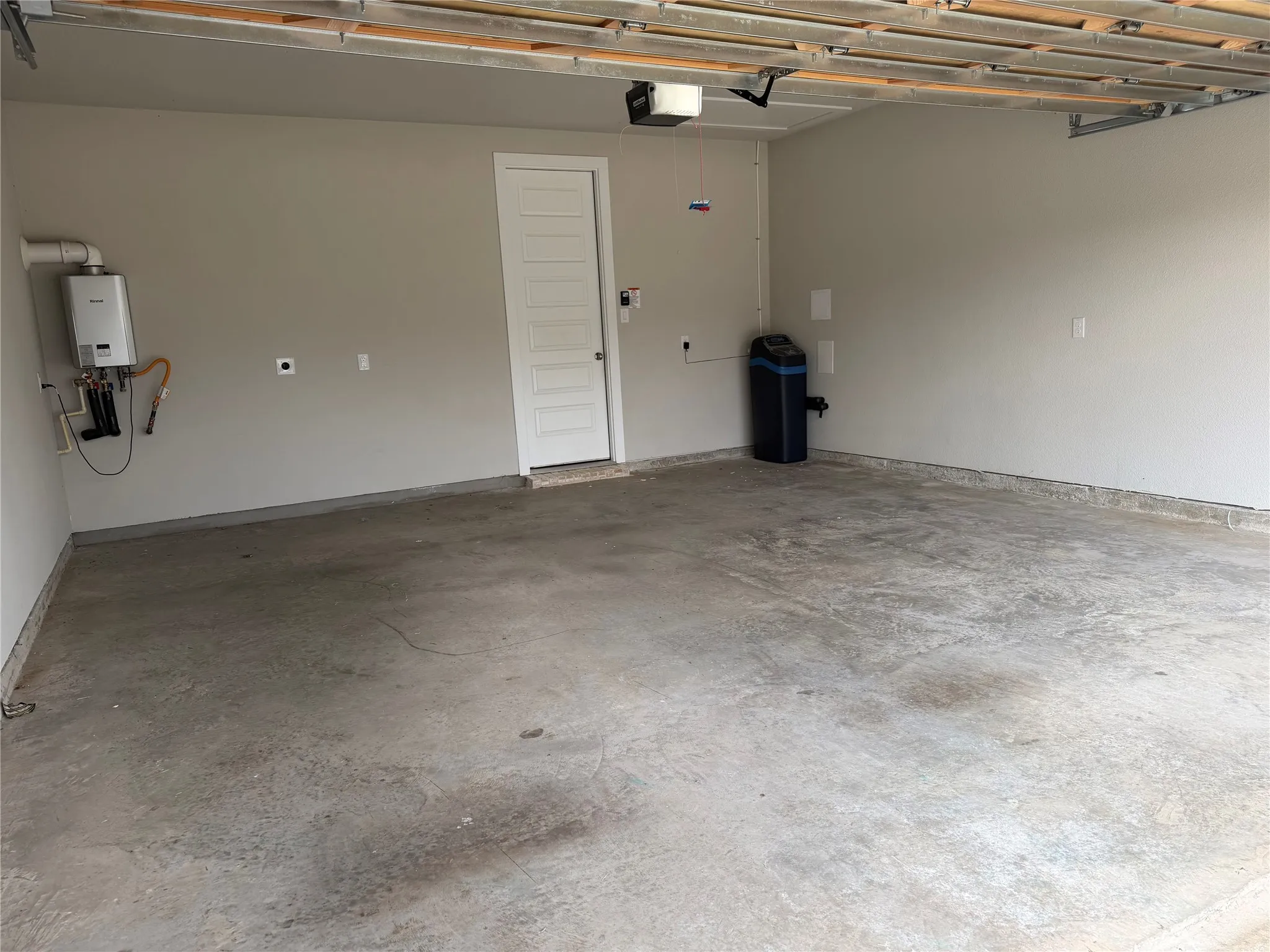 Attached garage space featuring concrete flooring, a tankless water heater, and a water softening system