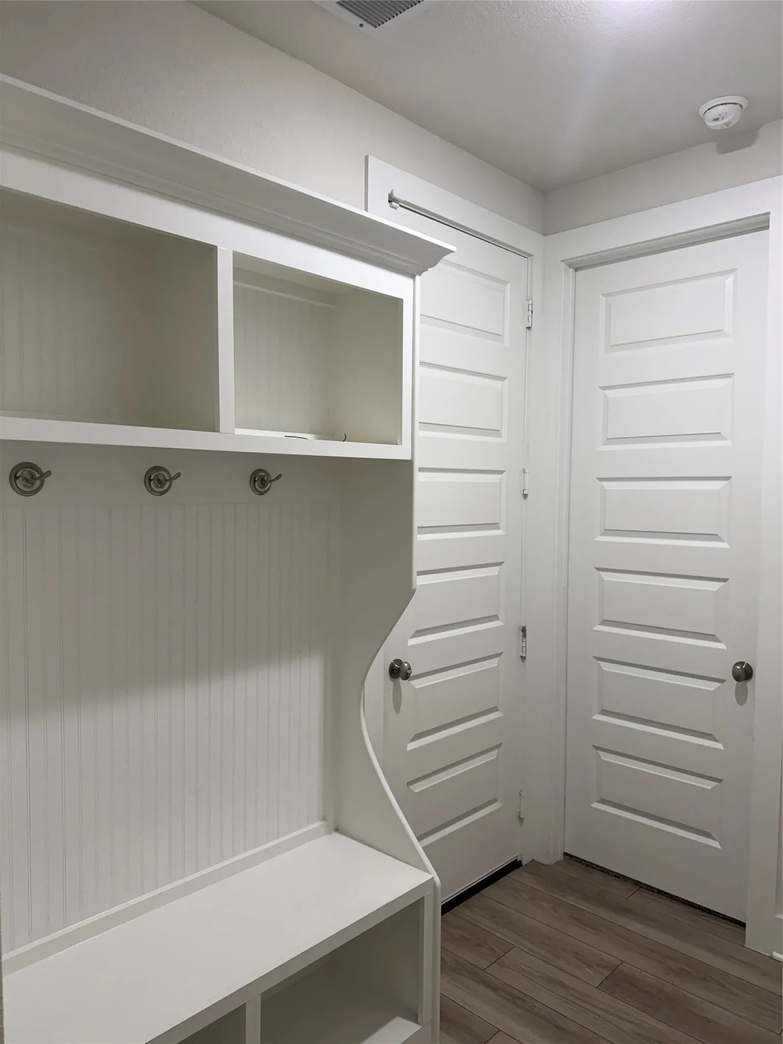 Built-in white mudroom bench with cubbies, upper shelving, and beadboard paneling