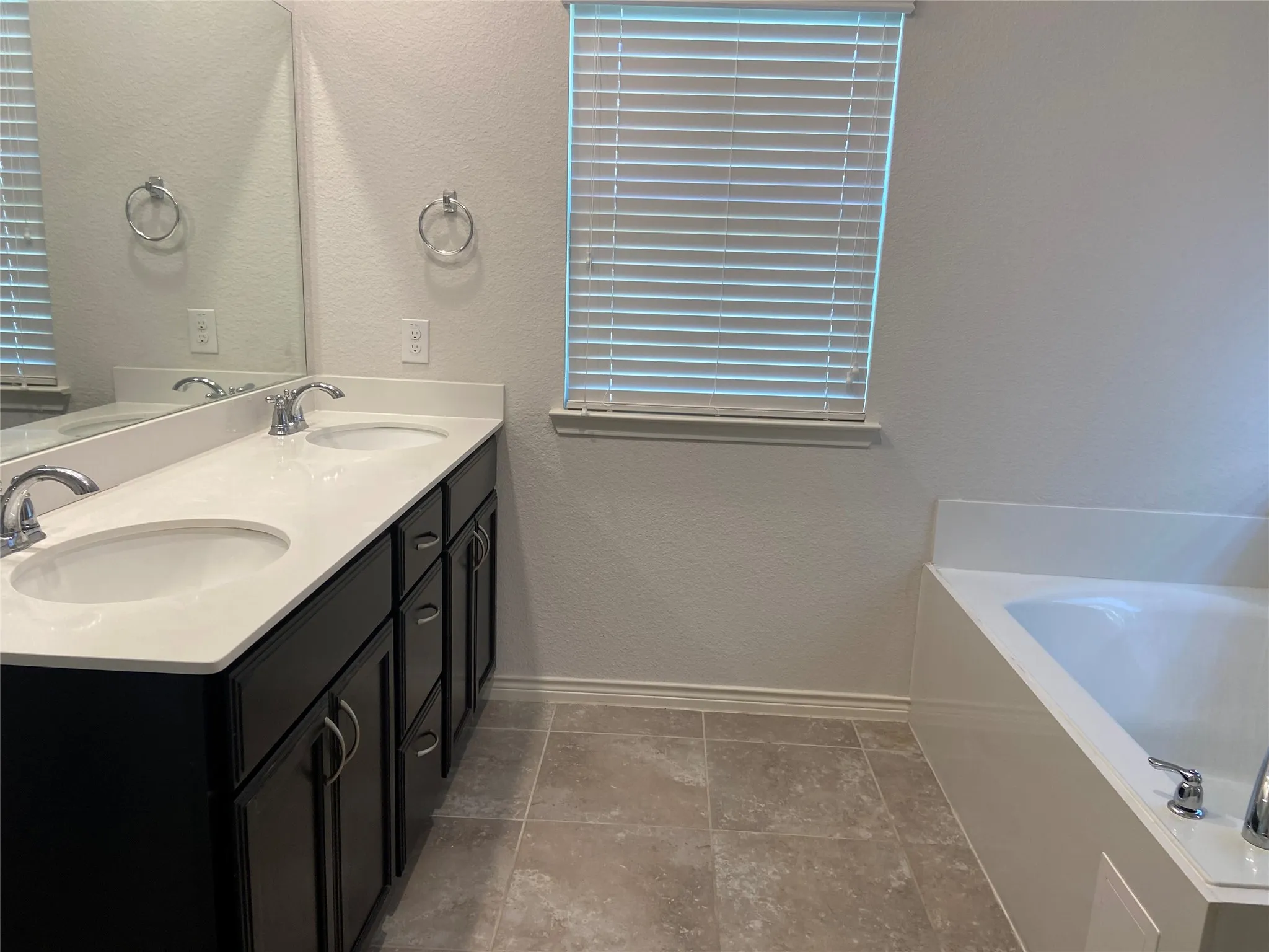 Full bathroom with a textured wall, a bath, double vanity, and light tile patterned floors