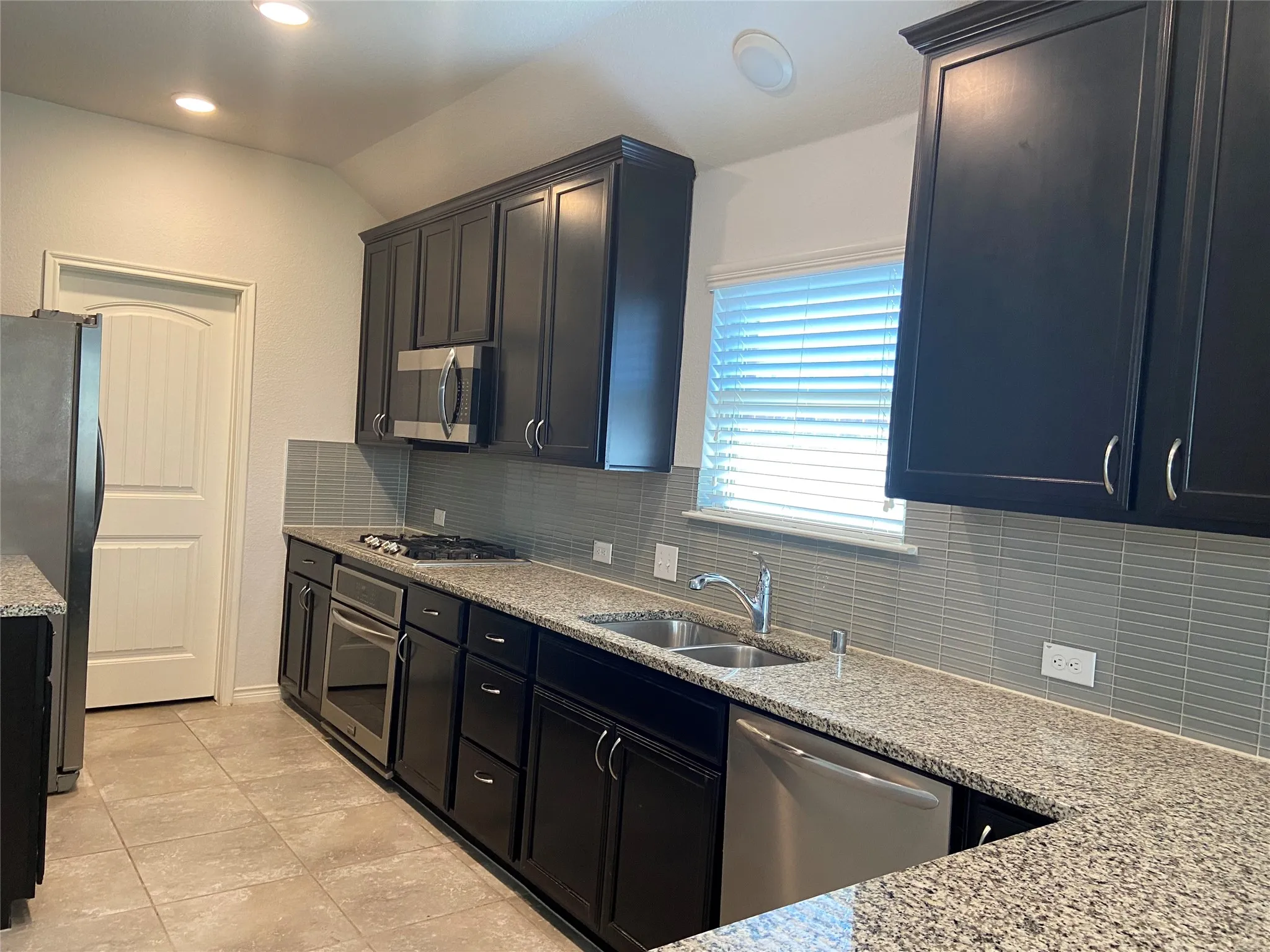 Kitchen with decorative backsplash, light stone counters, appliances with stainless steel finishes, recessed lighting, and dark cabinetry