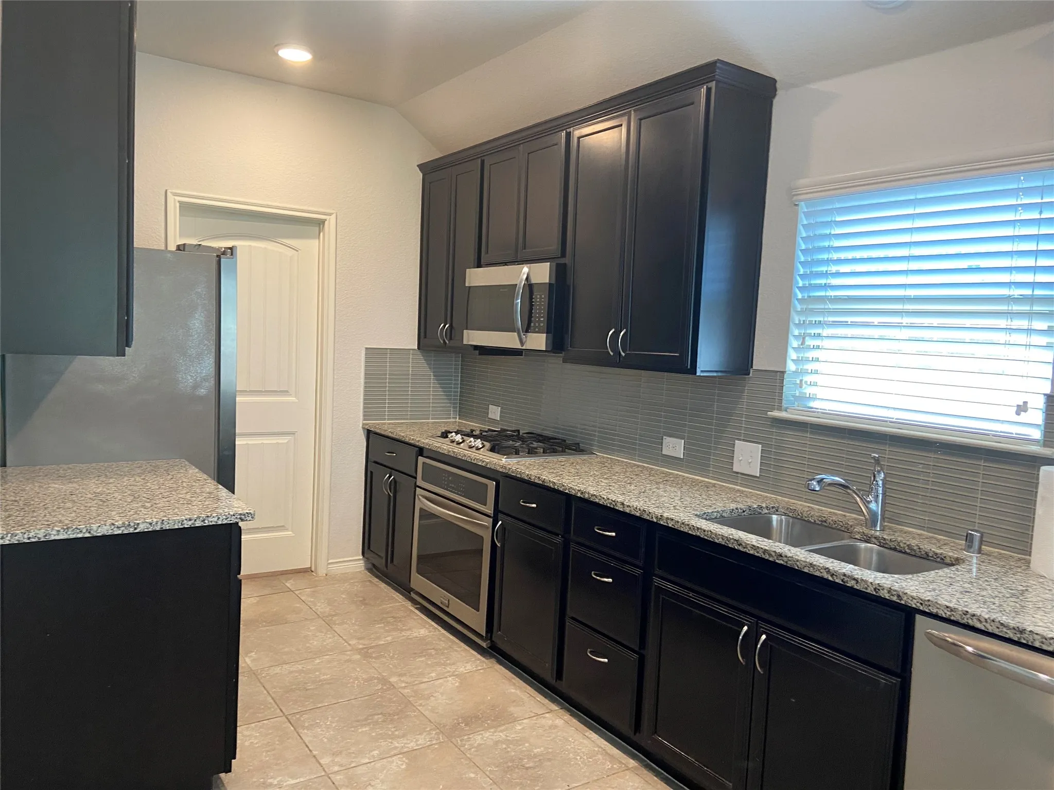 Kitchen featuring backsplash, light stone countertops, dark cabinets, and vaulted ceiling