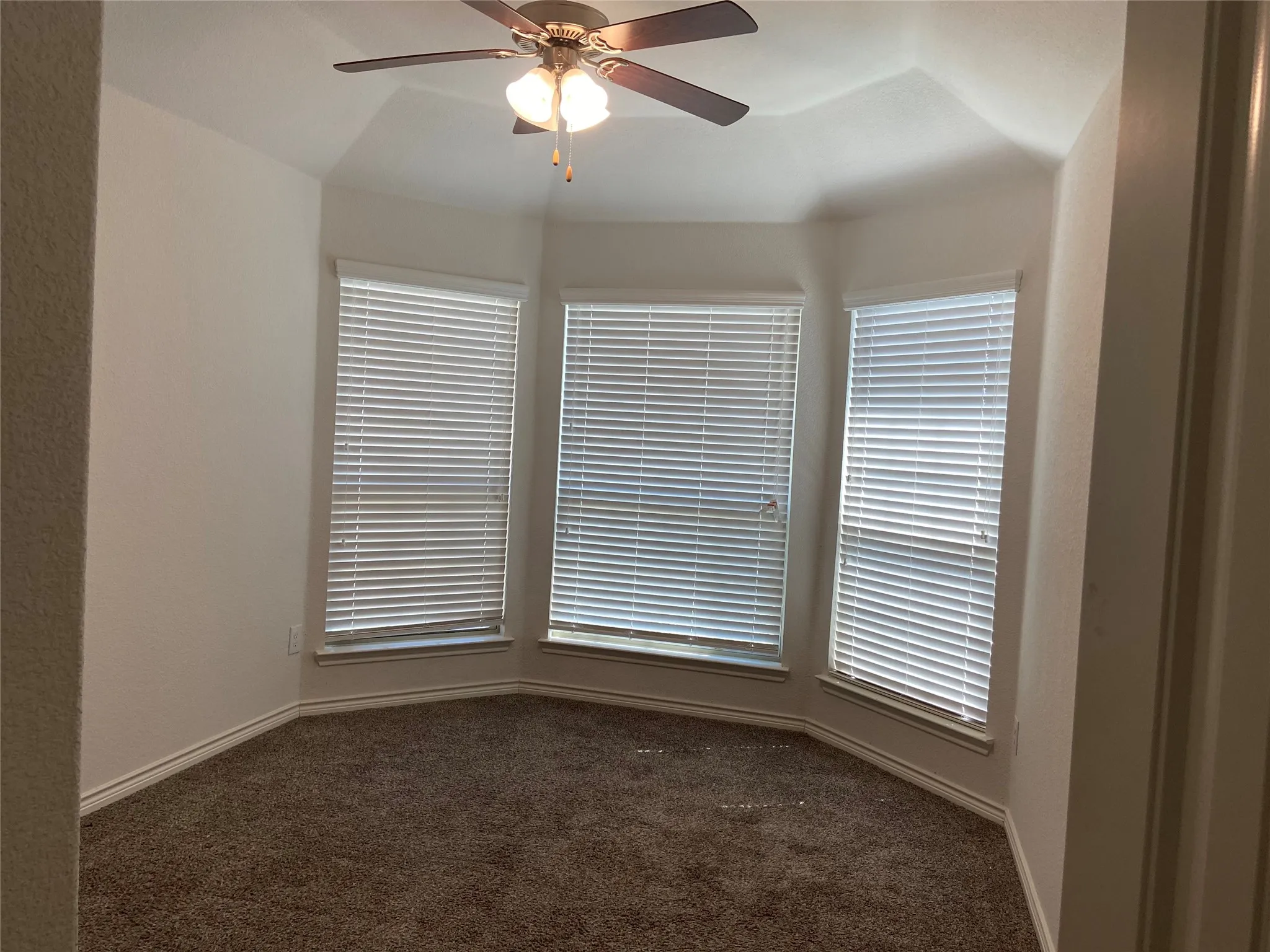 Spare room with dark colored carpet, a ceiling fan, and plenty of natural light
