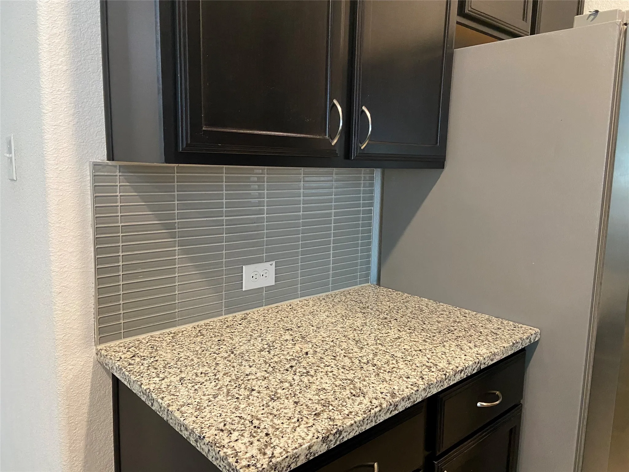 Detailed view of a textured wall, backsplash, and freestanding refrigerator