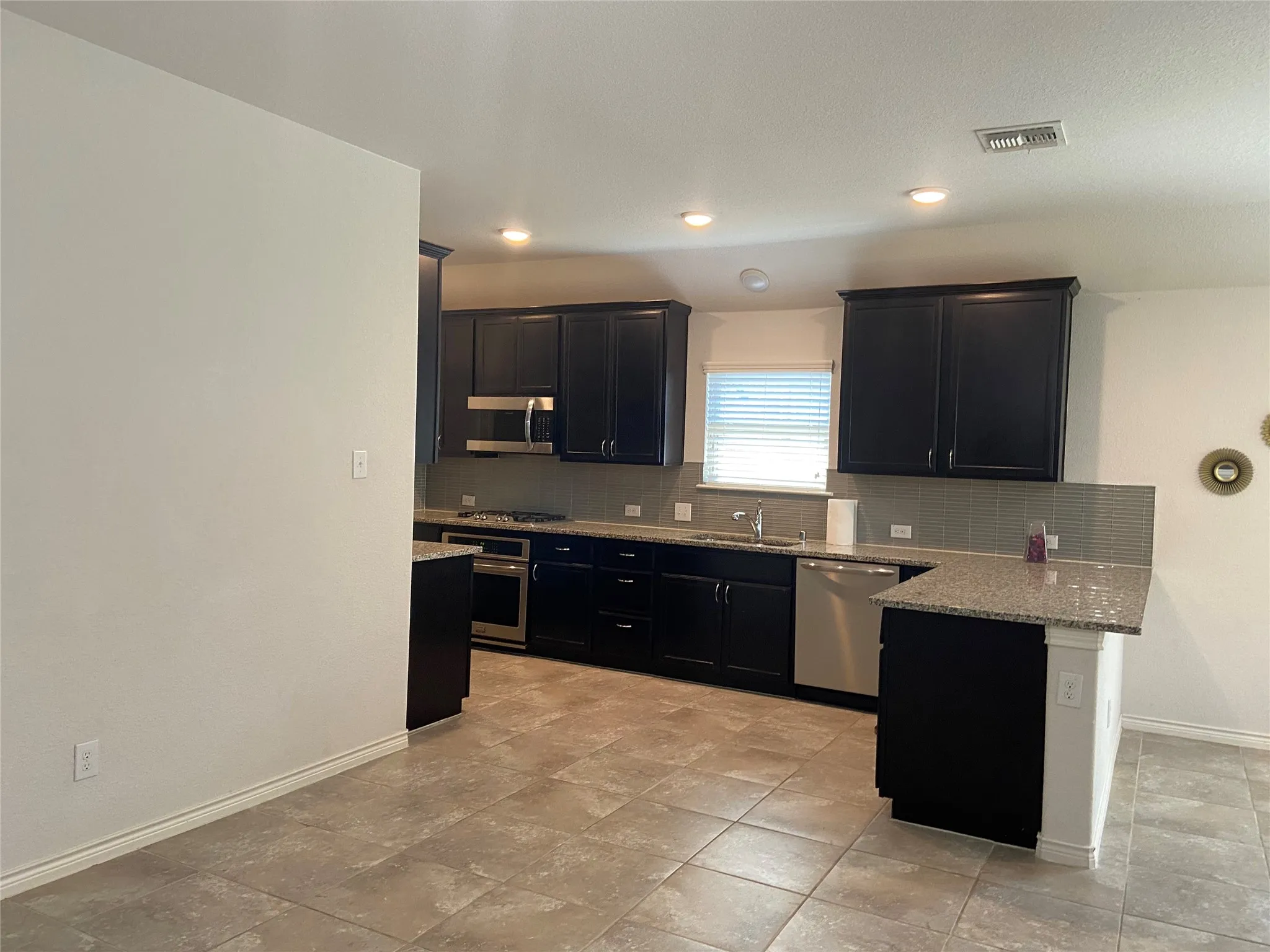 Kitchen with light stone counters, decorative backsplash, dark cabinetry, a peninsula, and appliances with stainless steel finishes