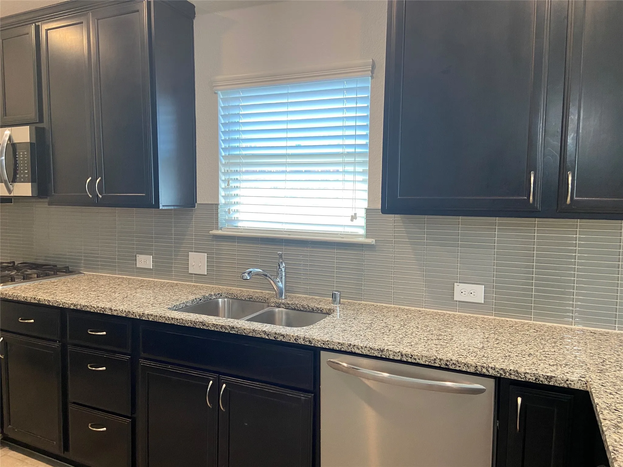 Kitchen with dark cabinets, appliances with stainless steel finishes, and light stone countertops