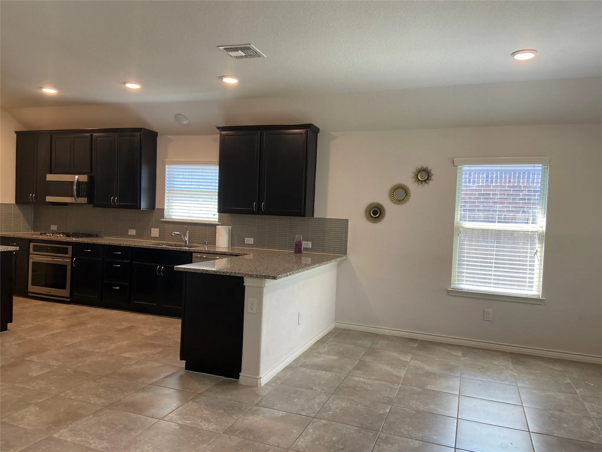 Kitchen with backsplash, light stone counters, stainless steel appliances, dark cabinets, and recessed lighting