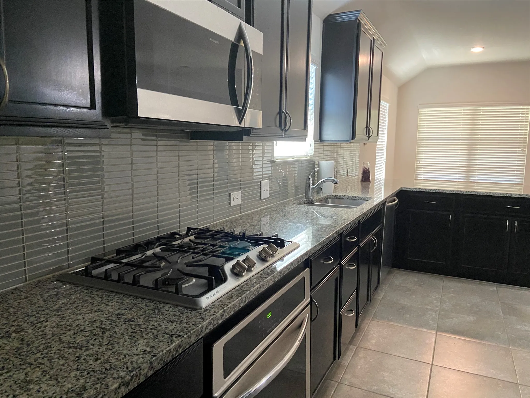 Kitchen featuring dark cabinetry, backsplash, appliances with stainless steel finishes, dark stone counters, and lofted ceiling
