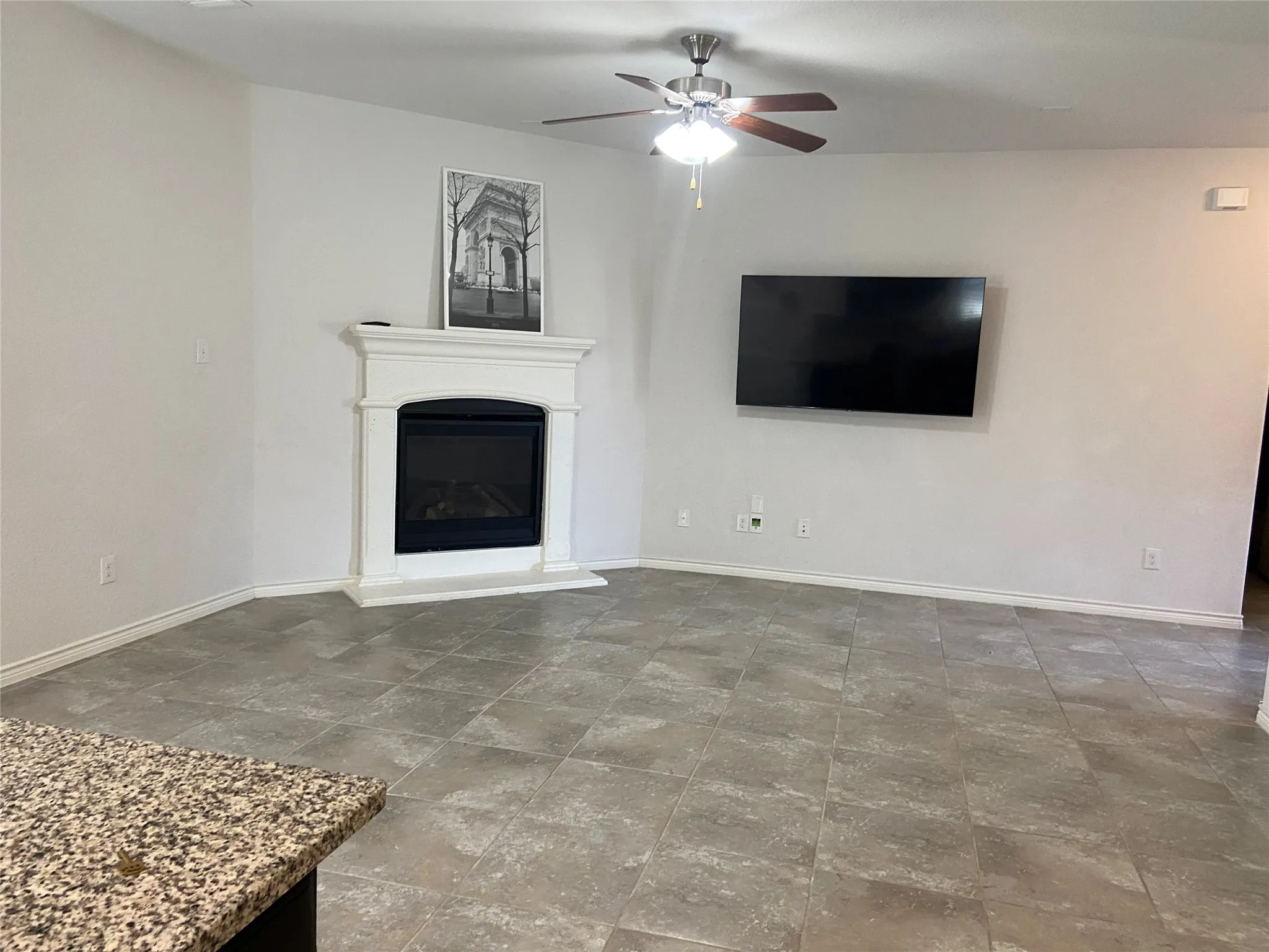 Unfurnished living room with a glass covered fireplace, ceiling fan, and stone finish floors