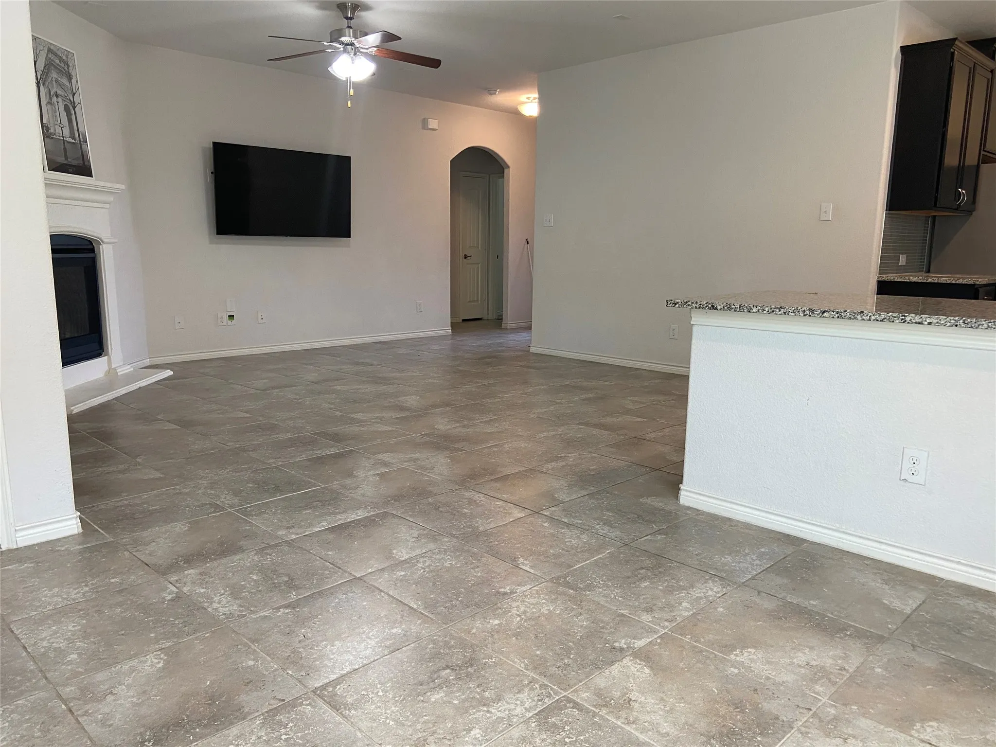 Unfurnished living room featuring arched walkways, a glass covered fireplace, and ceiling fan