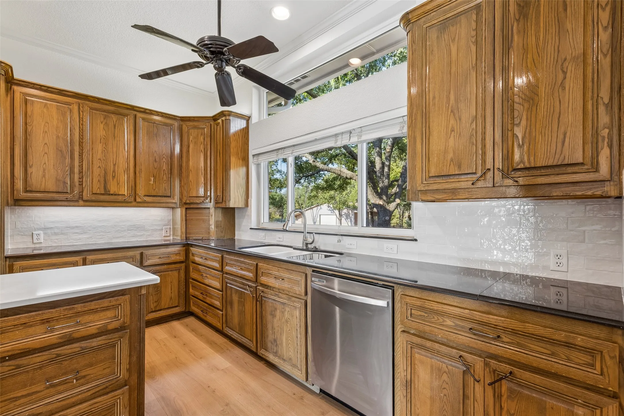 Kitchen featuring wood cabinetry, stone countertops, a stainless steel dishwasher, and a ceiling fan