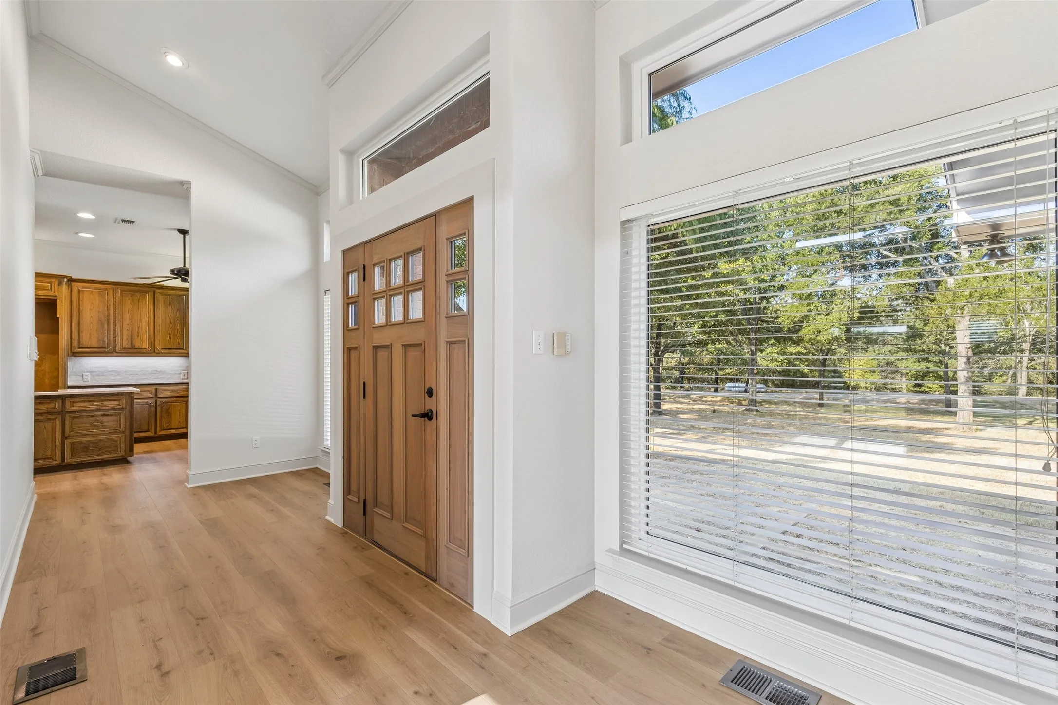 Wood-finish flooring, vaulted ceiling, wood-paneled entry door with glass inserts, transom window, and large window with horizontal blinds