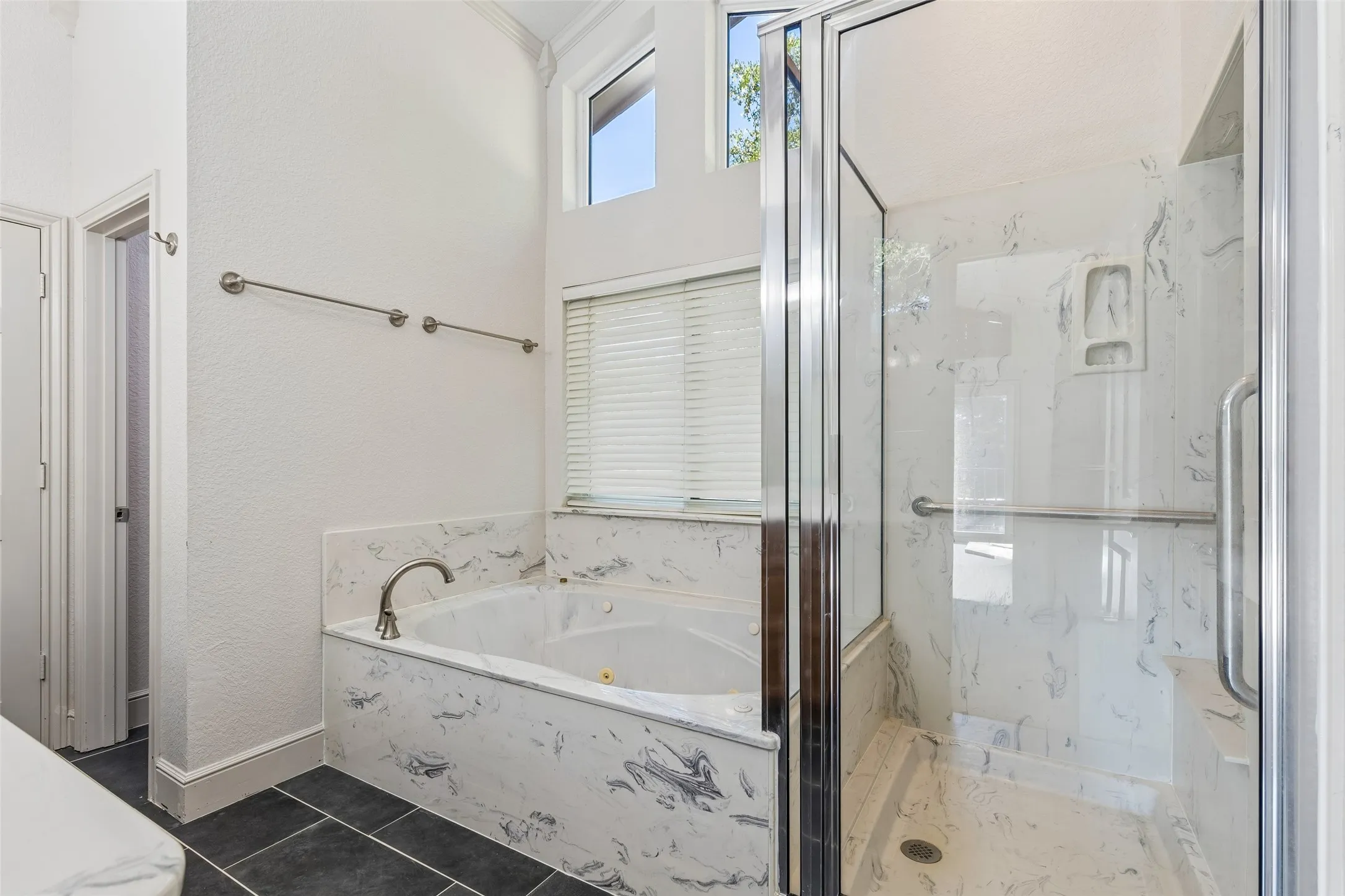Soaking tub with a polished nickel faucet, glass-enclosed shower with a built-in bench, and high transom windows