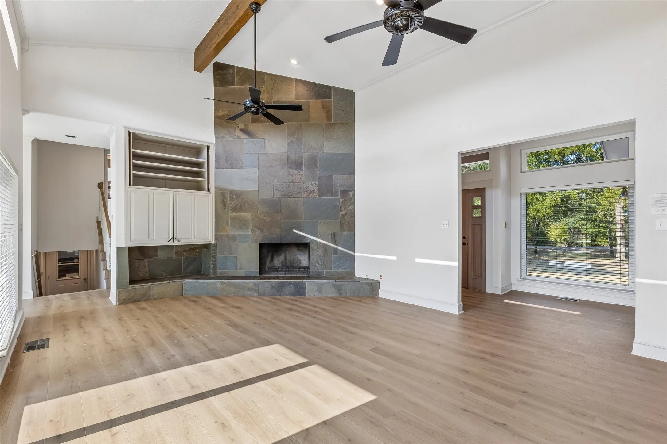 Vaulted ceilings with exposed wood beam, full-height stone fireplace, built-in cabinetry, wood-finish flooring, and expansive windows